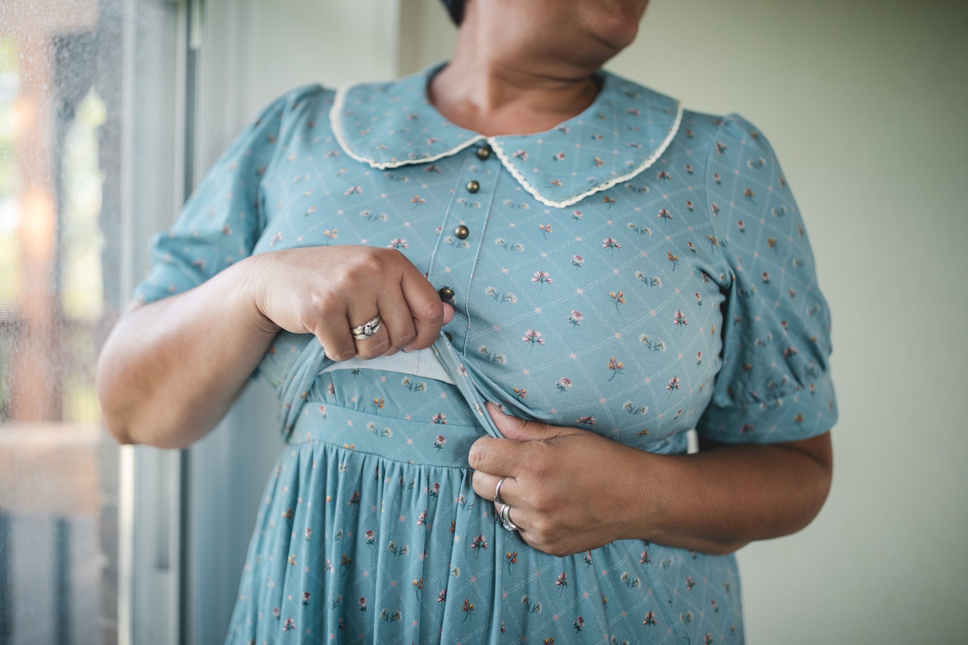 Person wearing a blue modest nursing dress with a floral pattern, standing indoors.
