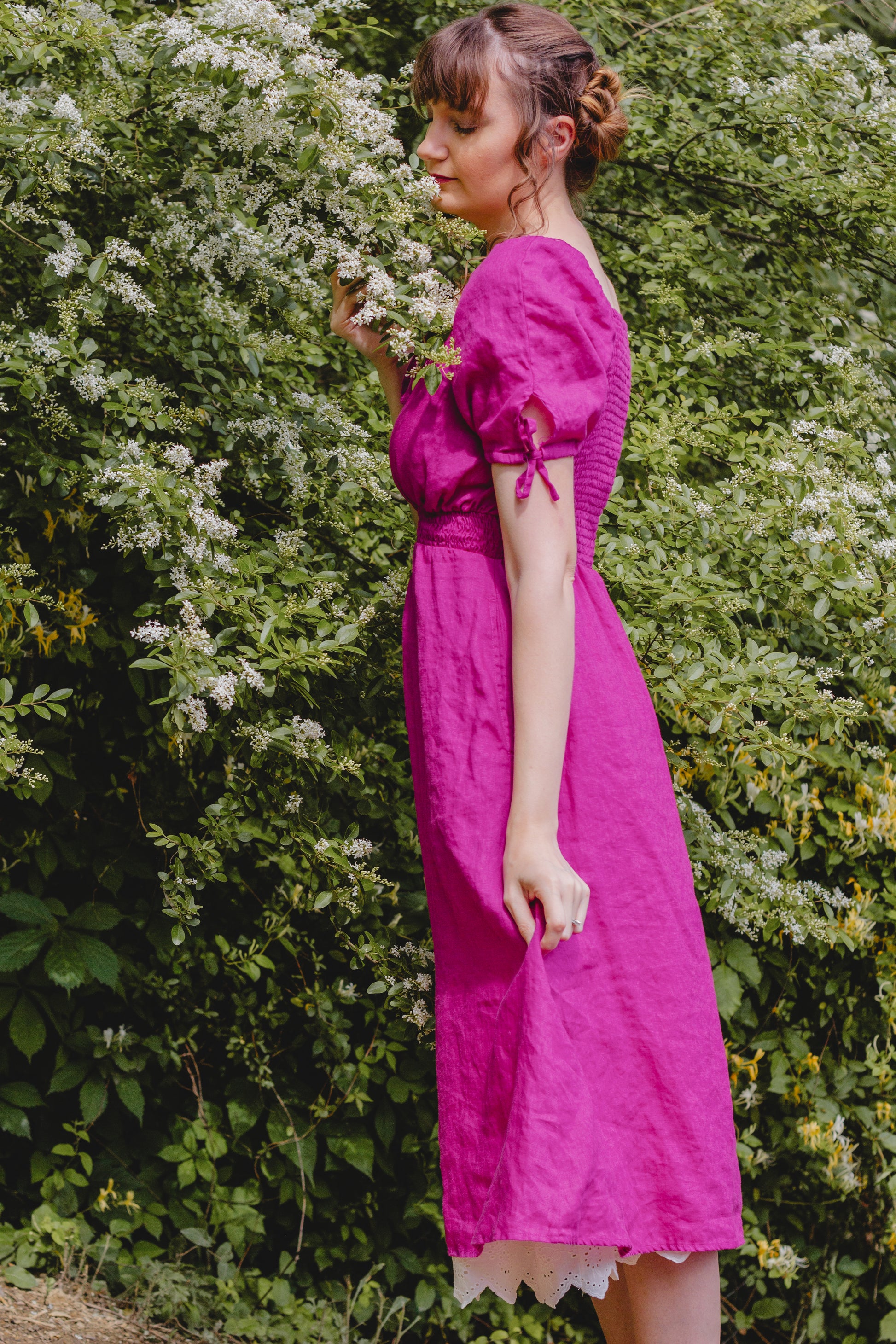 Woman in a pink modest nursing dress standing in front of green foliage