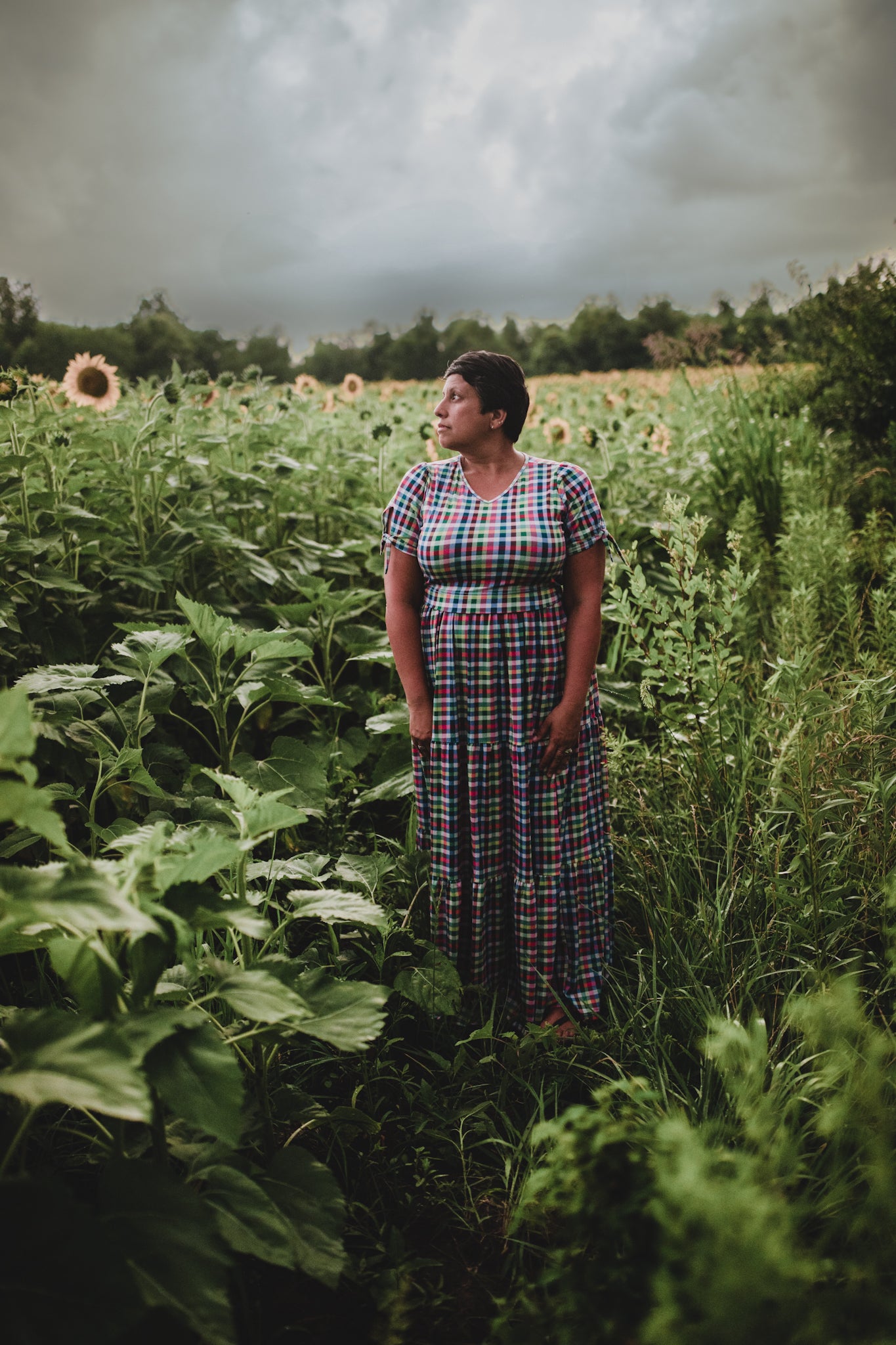 Woman standing in a sunflower field with a stormy sky in a modest nursing dress.