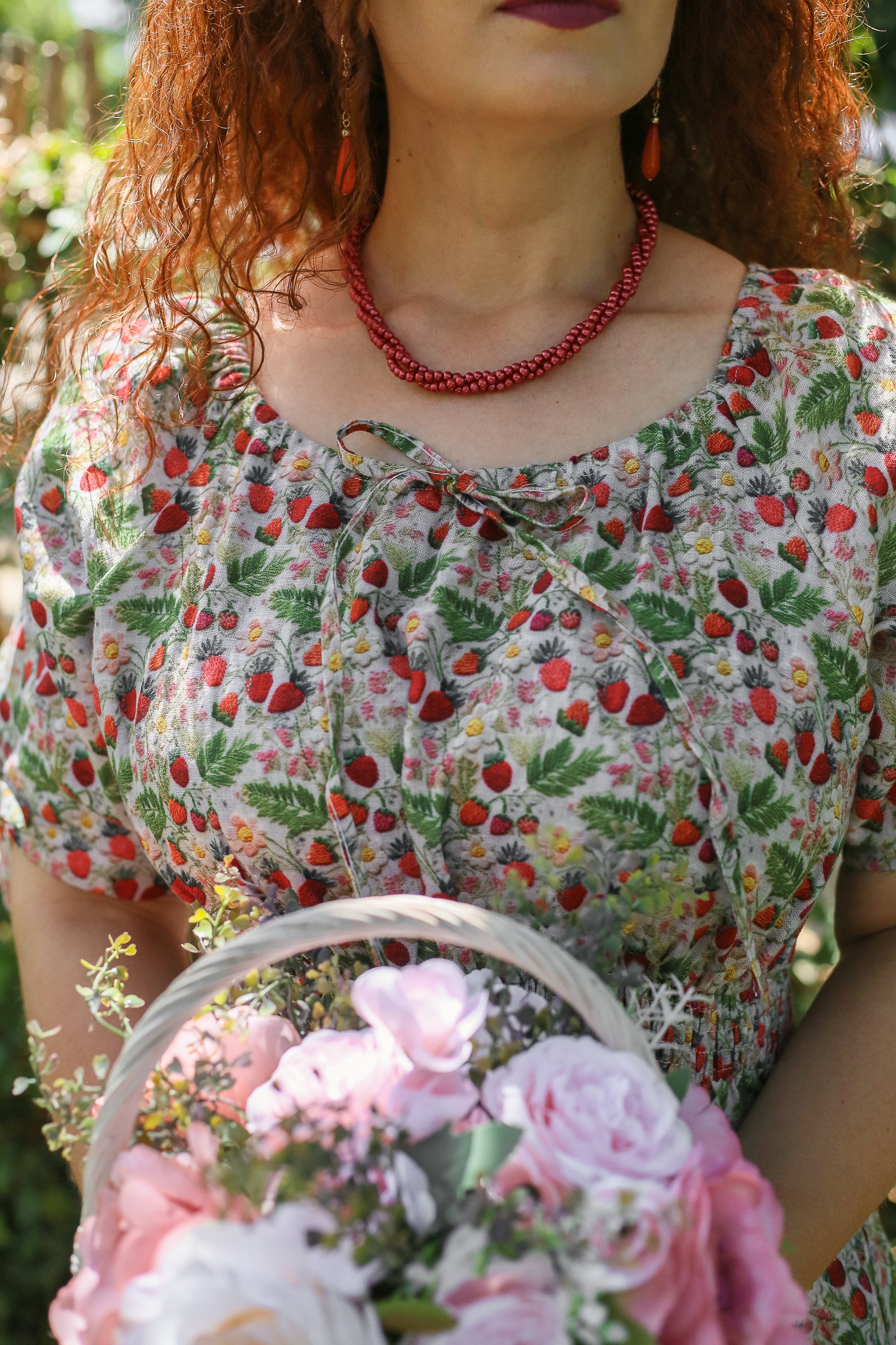 Woman wearing a floral modest nursing dress with a red necklace, holding a basket of flowers outdoors.