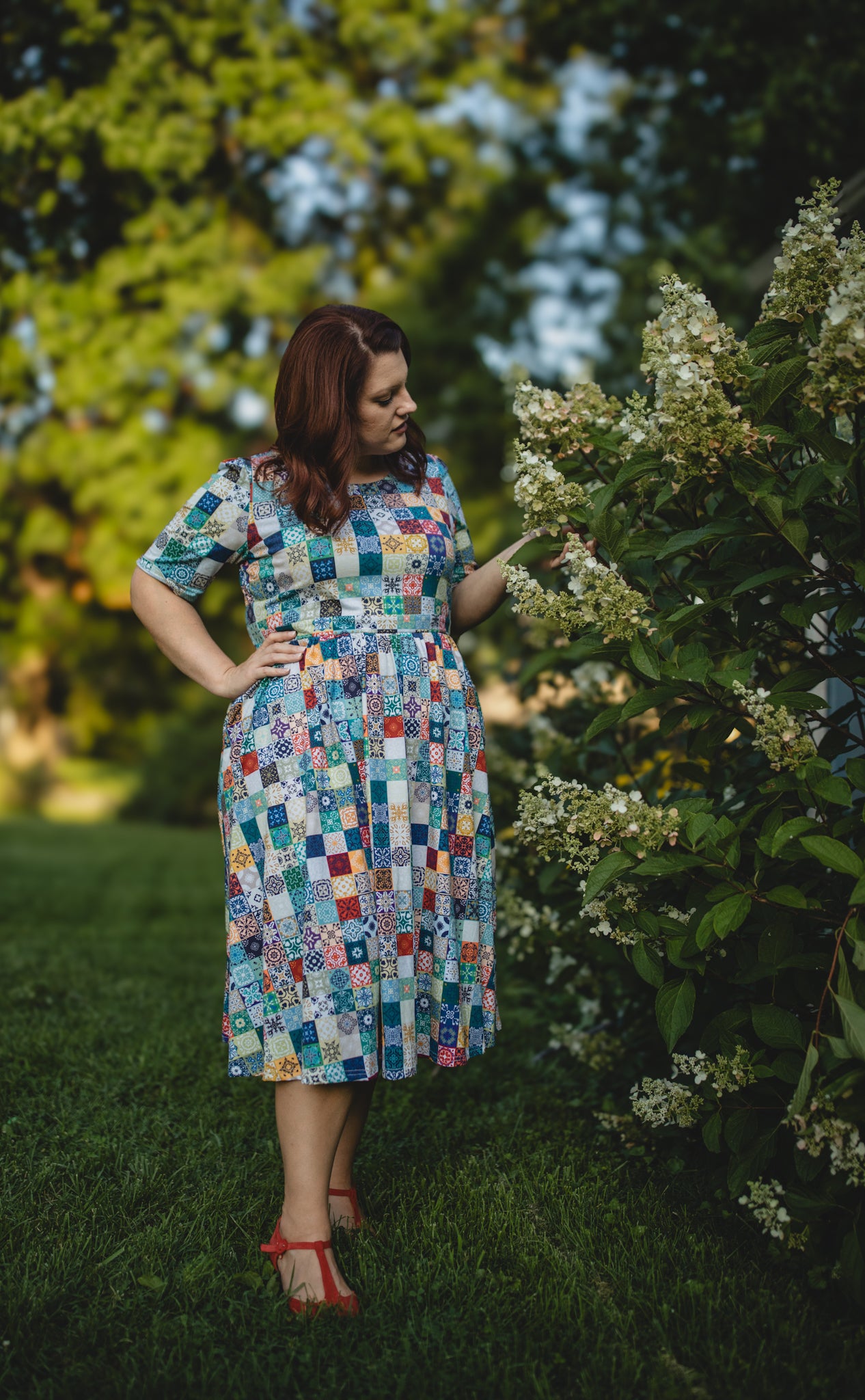 Woman in a colorful checkered modest nursing dress standing in a garden