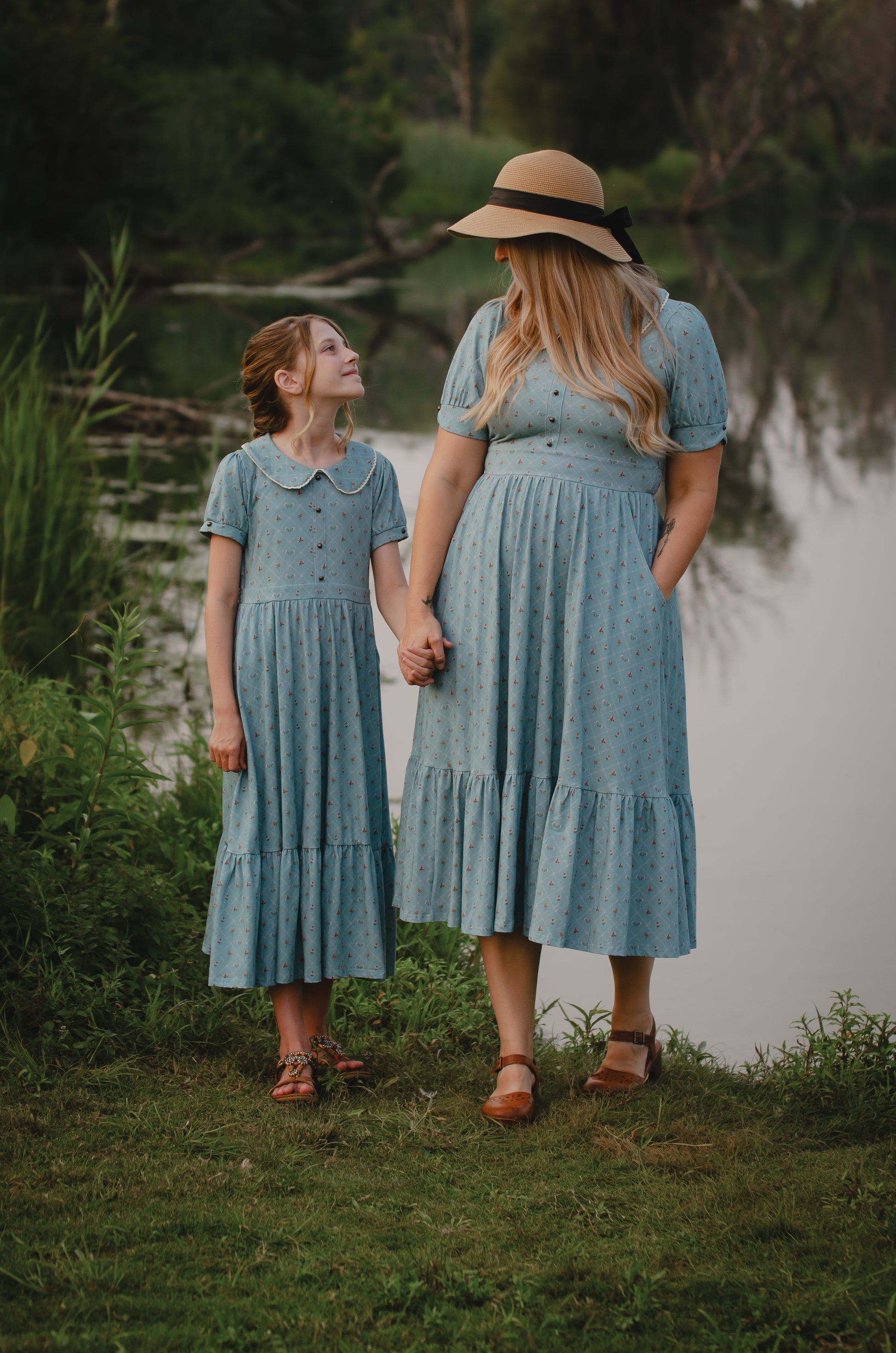 Mother and daughter in matching modest blue dresses standing by a body of water.