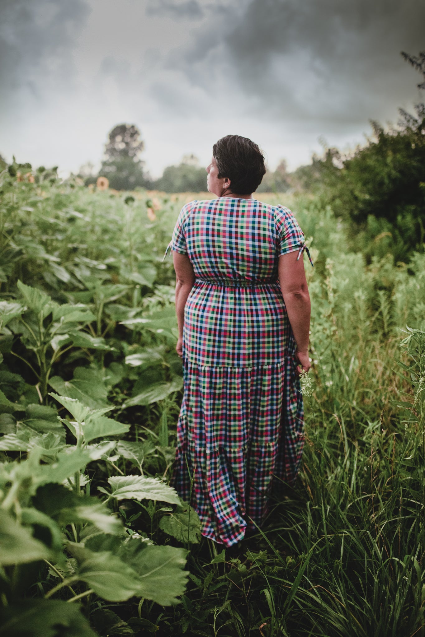 Person in a plaid modest nursing dress standing in a field with a stormy sky.