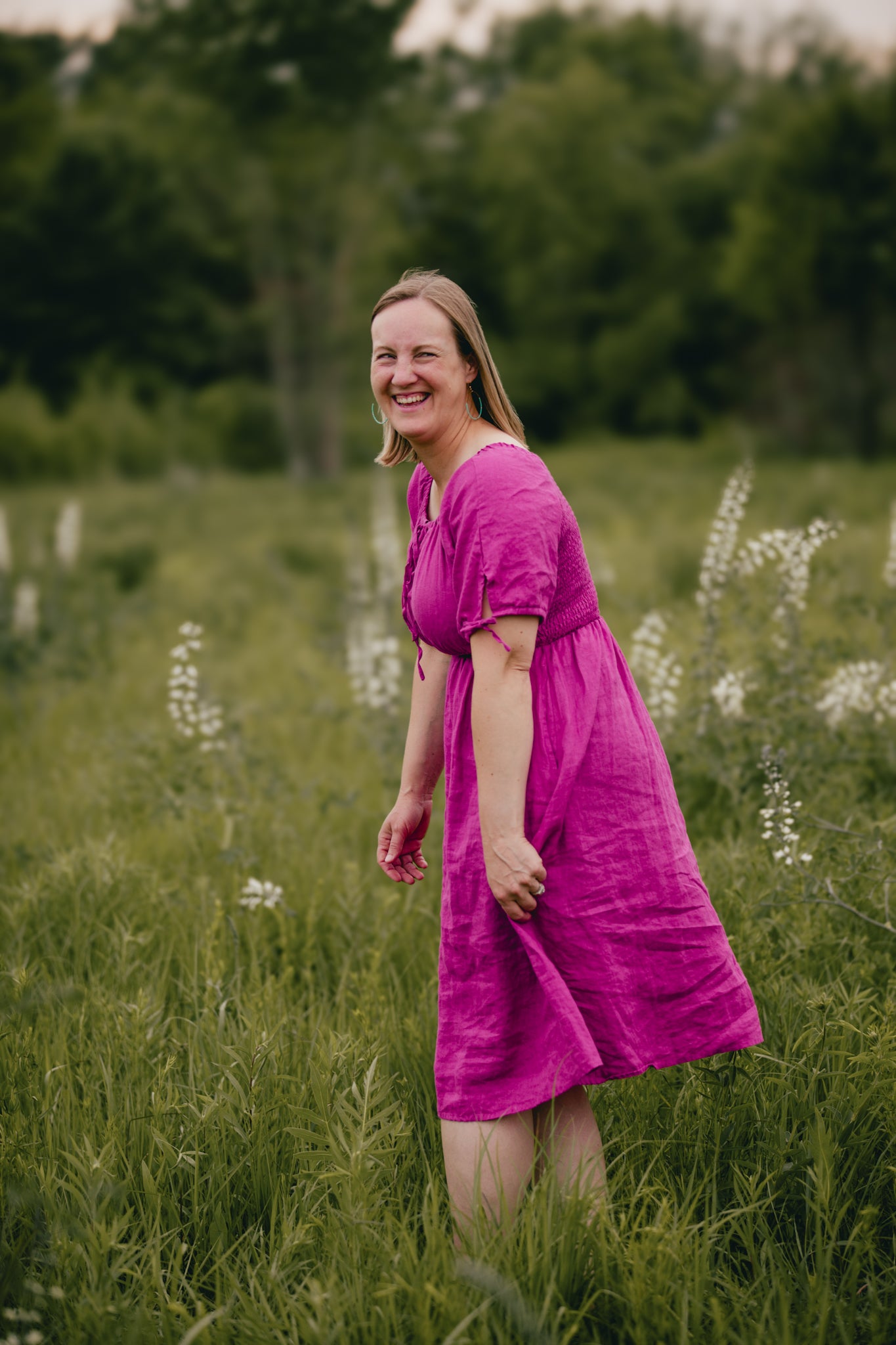Woman in a pink modest nursing dress standing in a field with greenery and wildflowers.