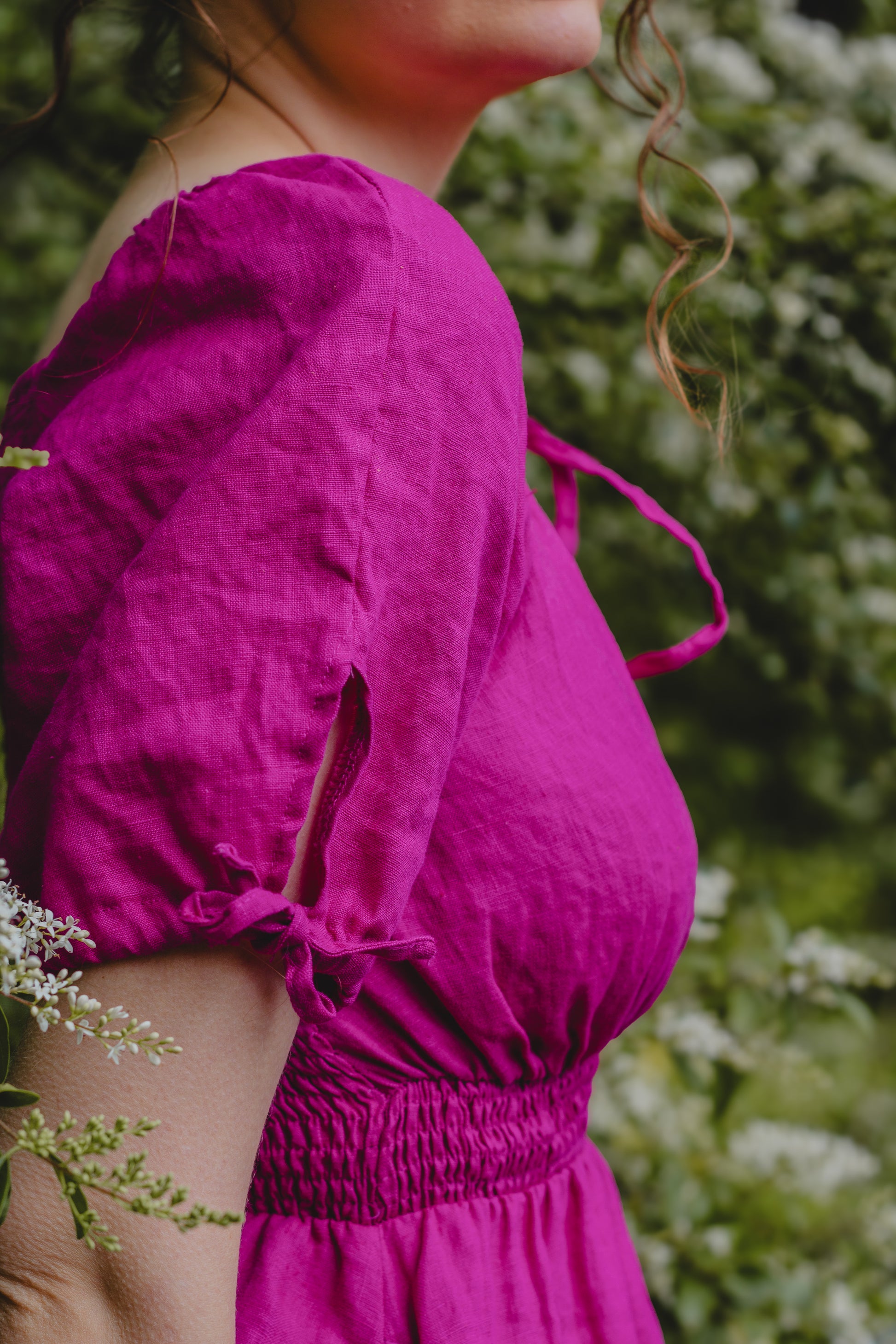 Person wearing a bright pink modest nursing dress with a blurred green background