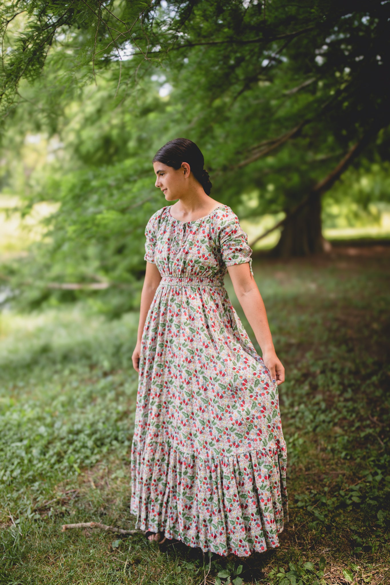 Woman in a floral modest nursing dress standing in a park with trees and grass.