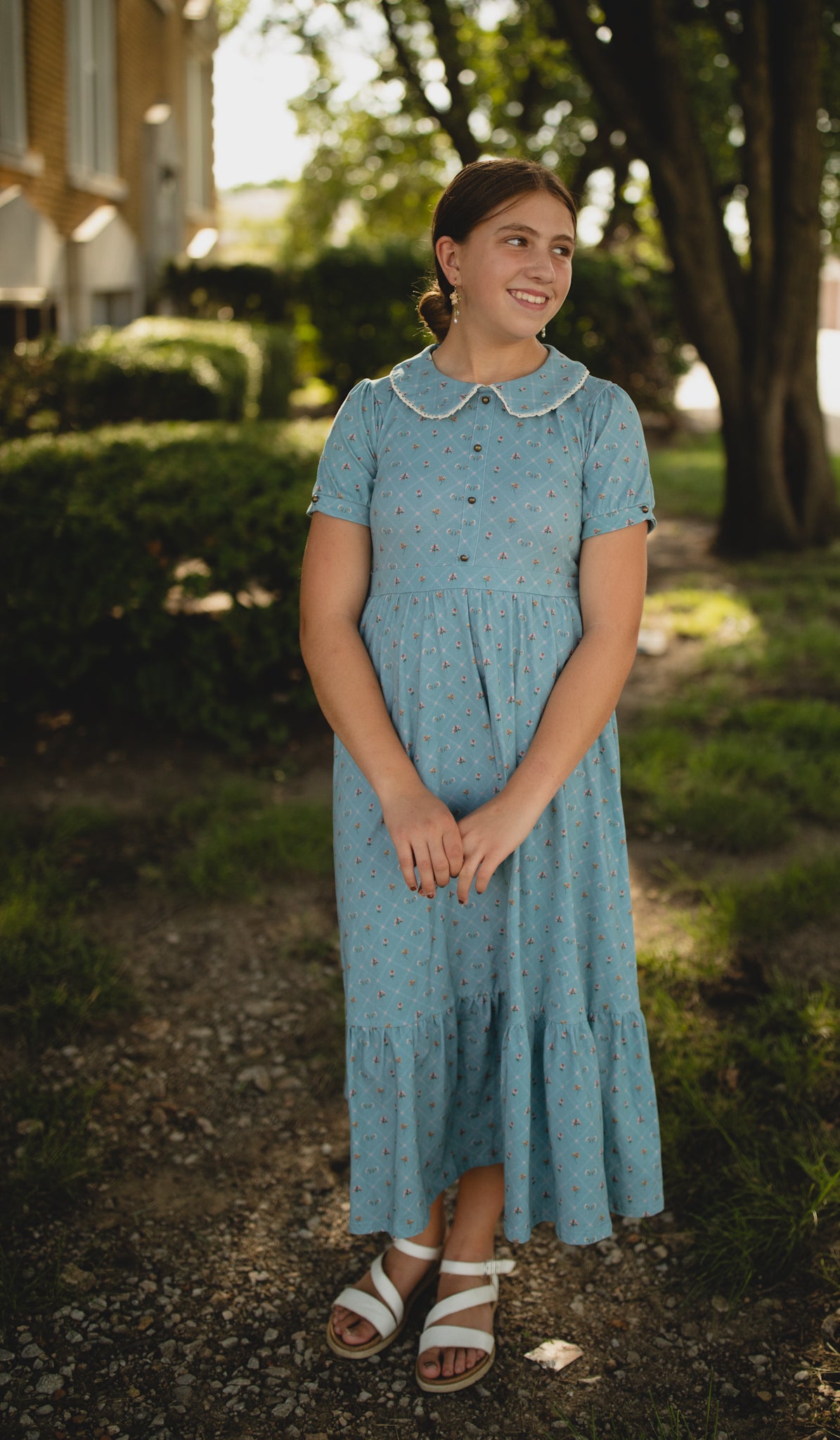 Woman in a blue modest dress standing outdoors with greenery around
