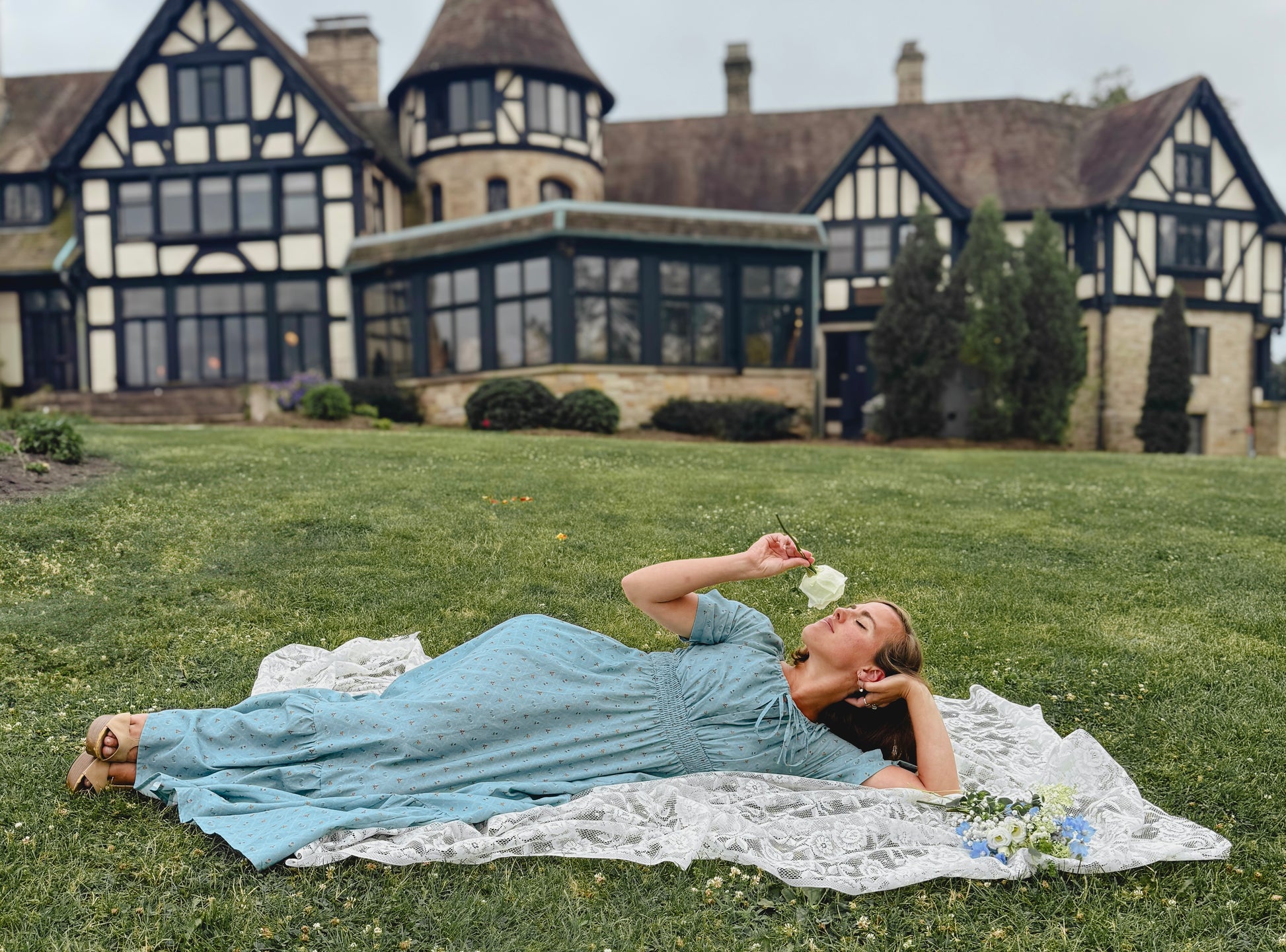 Woman in a blue modest nursing dress lying on a blanket in front of a large house