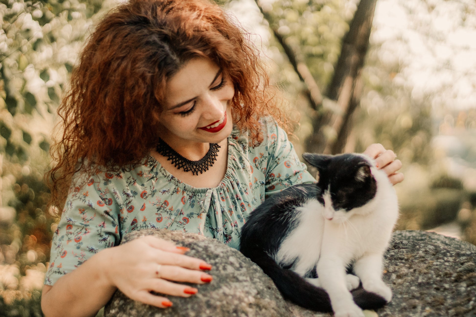 Woman with red hair holding a black and white cat outdoors
