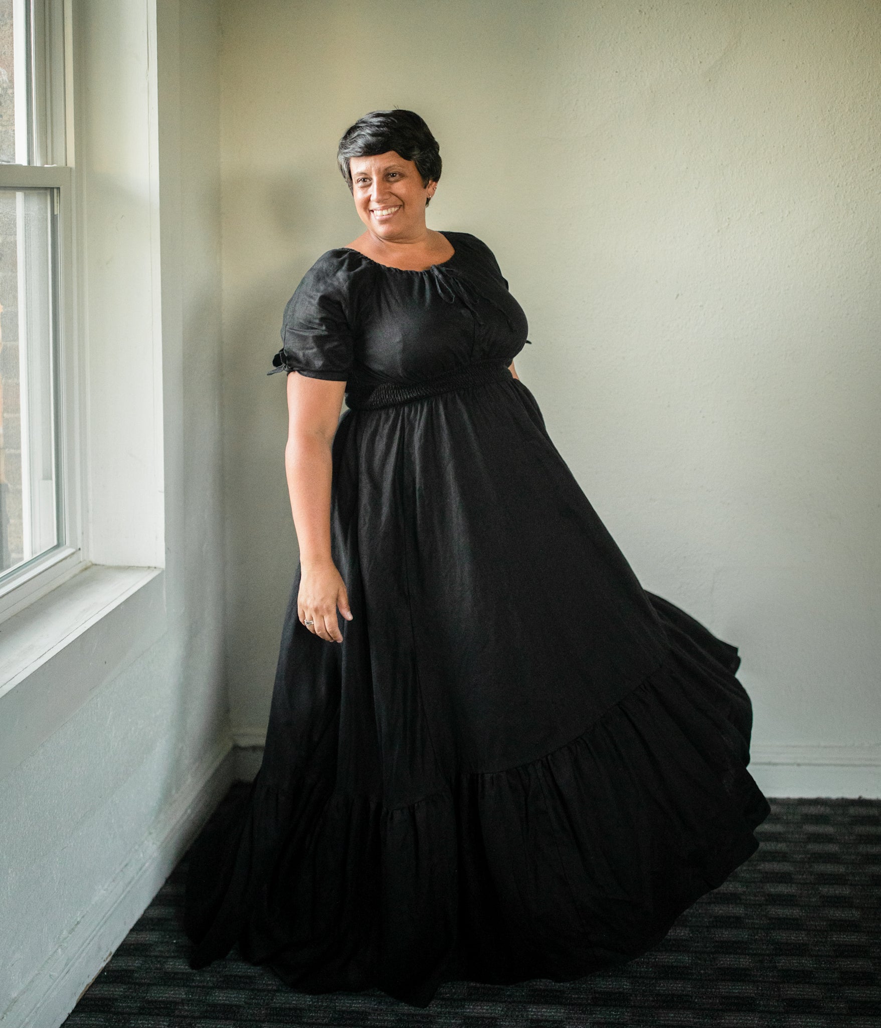 Woman in a black modest nursing dress standing in a room with a window.