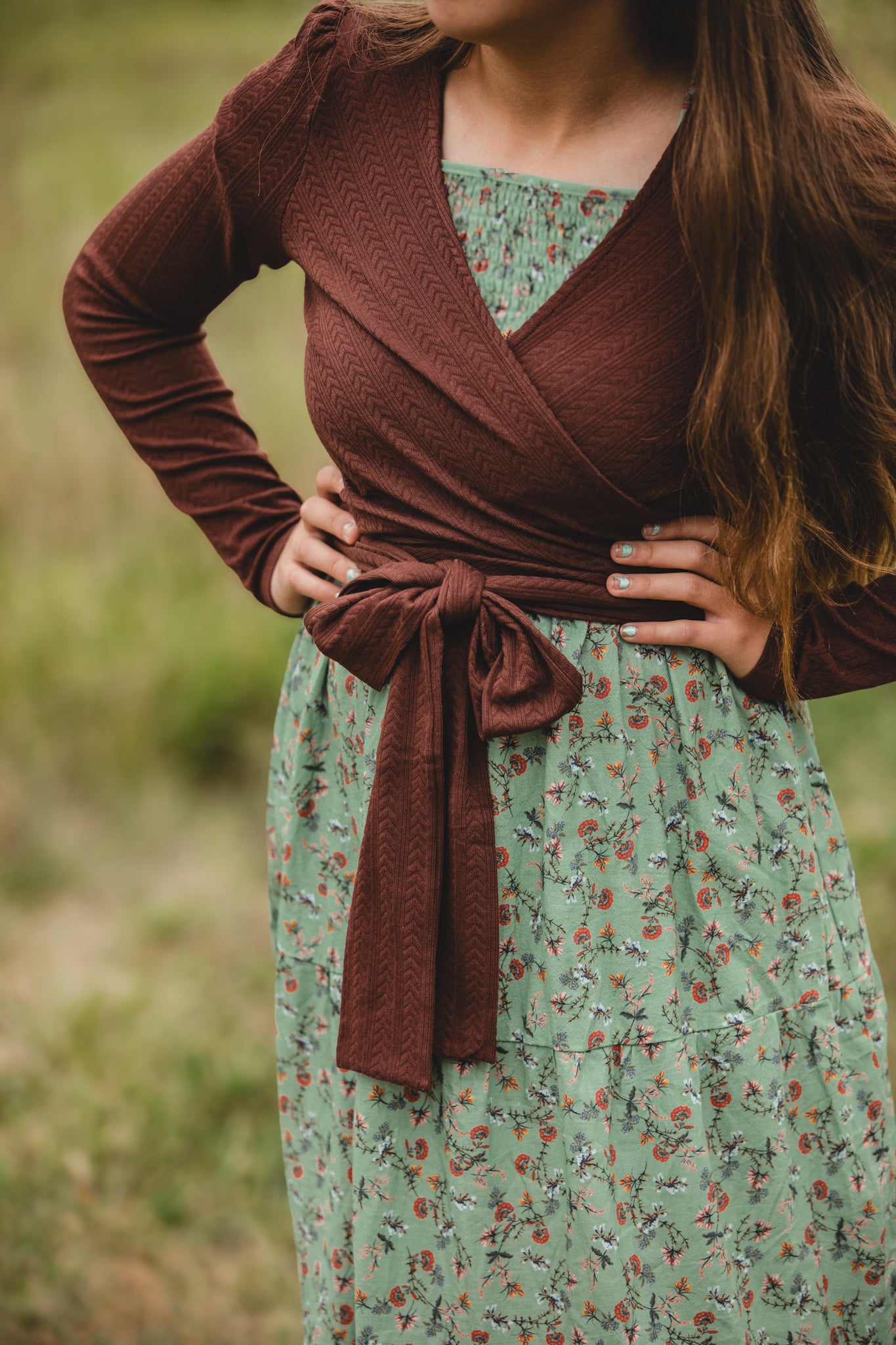 Woman wearing a brown cardigan over a green floral dress in a natural setting