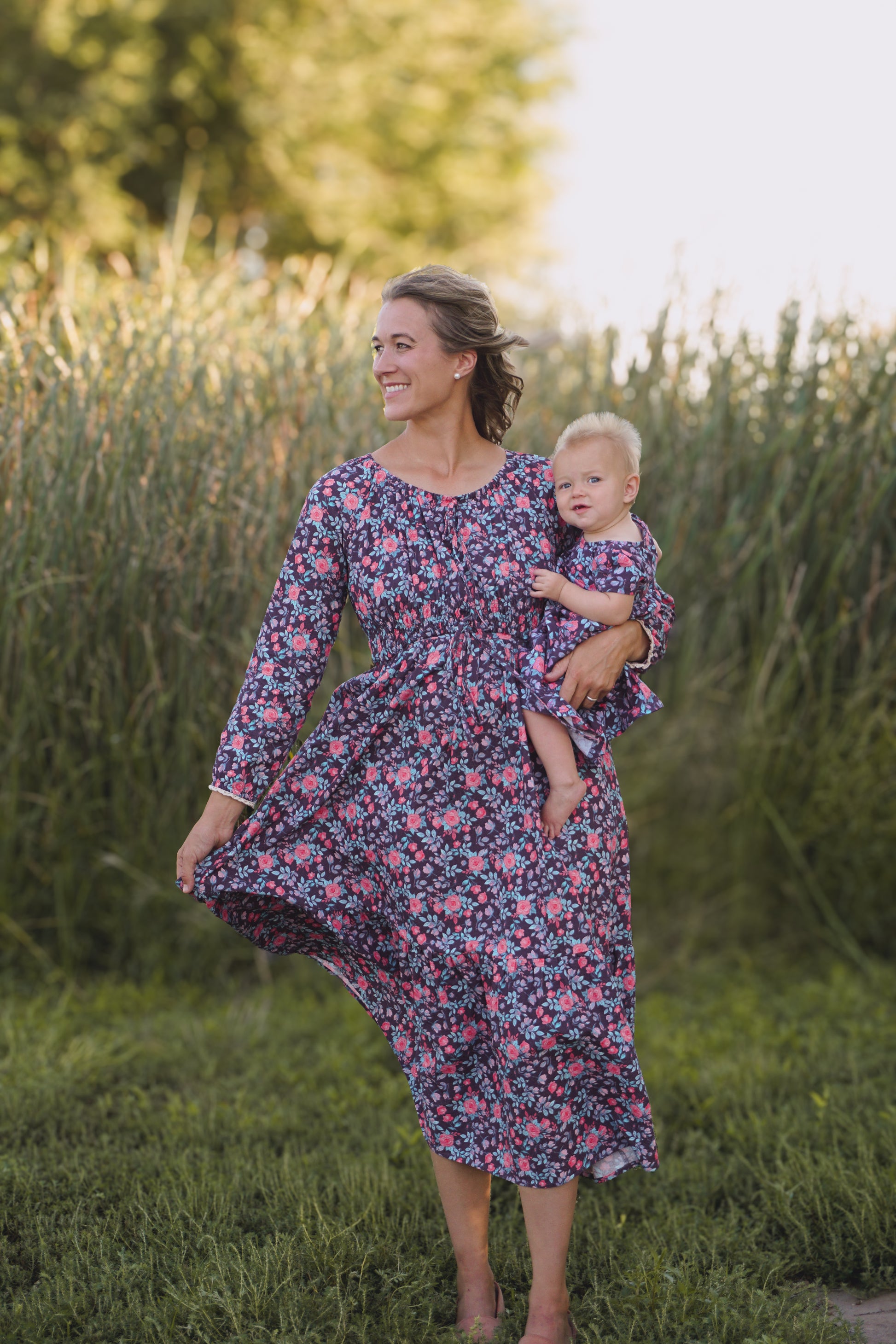 Woman in modest nursing floral dress holding baby in field