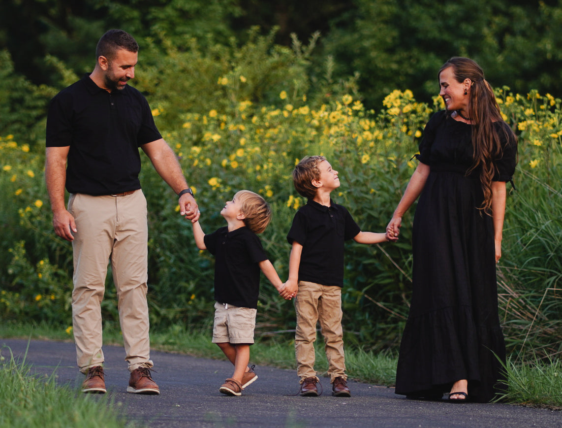 Family of four walking together on a path with yellow flowers and greenery in the background