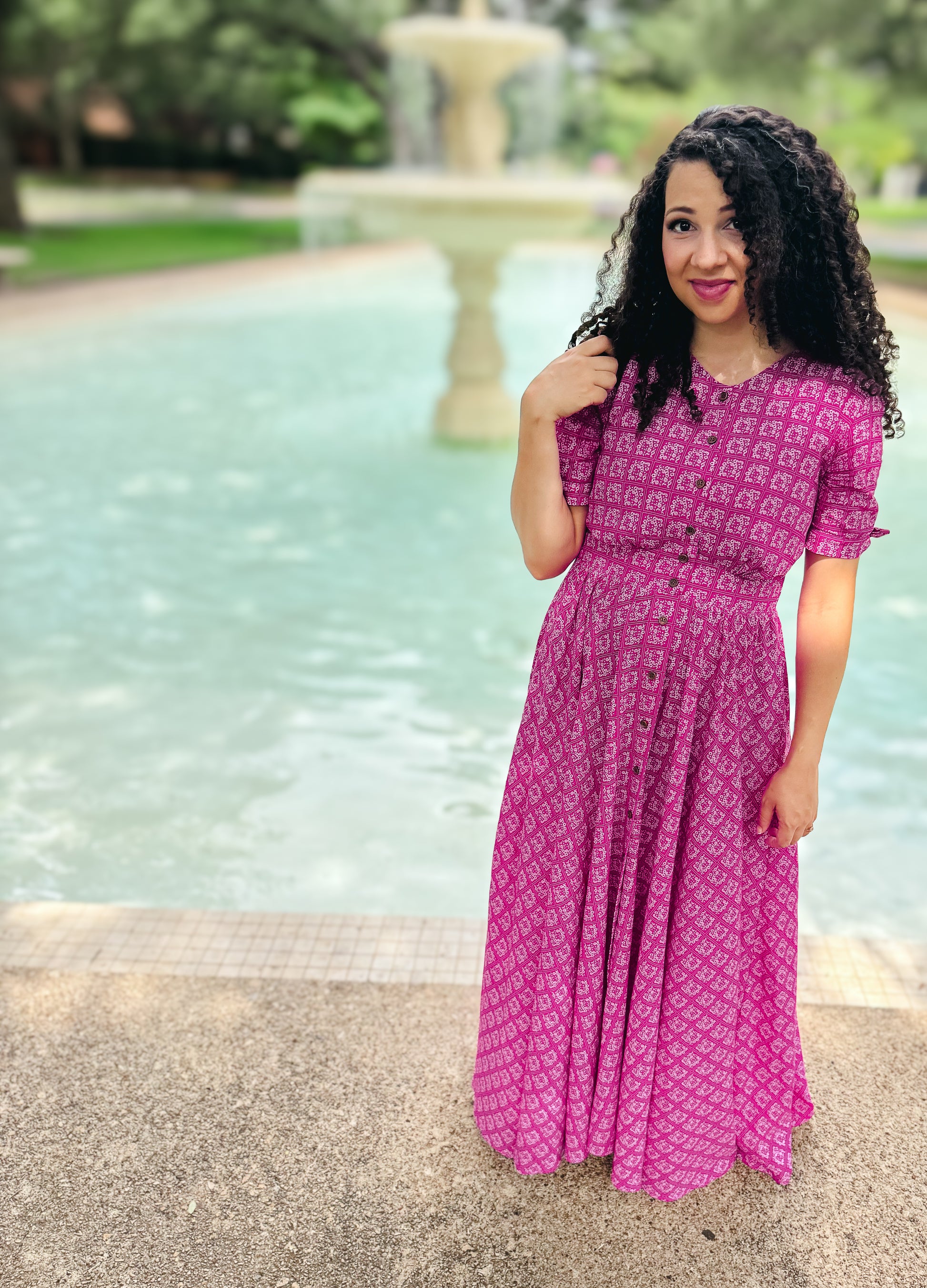 Woman in a pink modest nursing dress standing by a fountain in a park