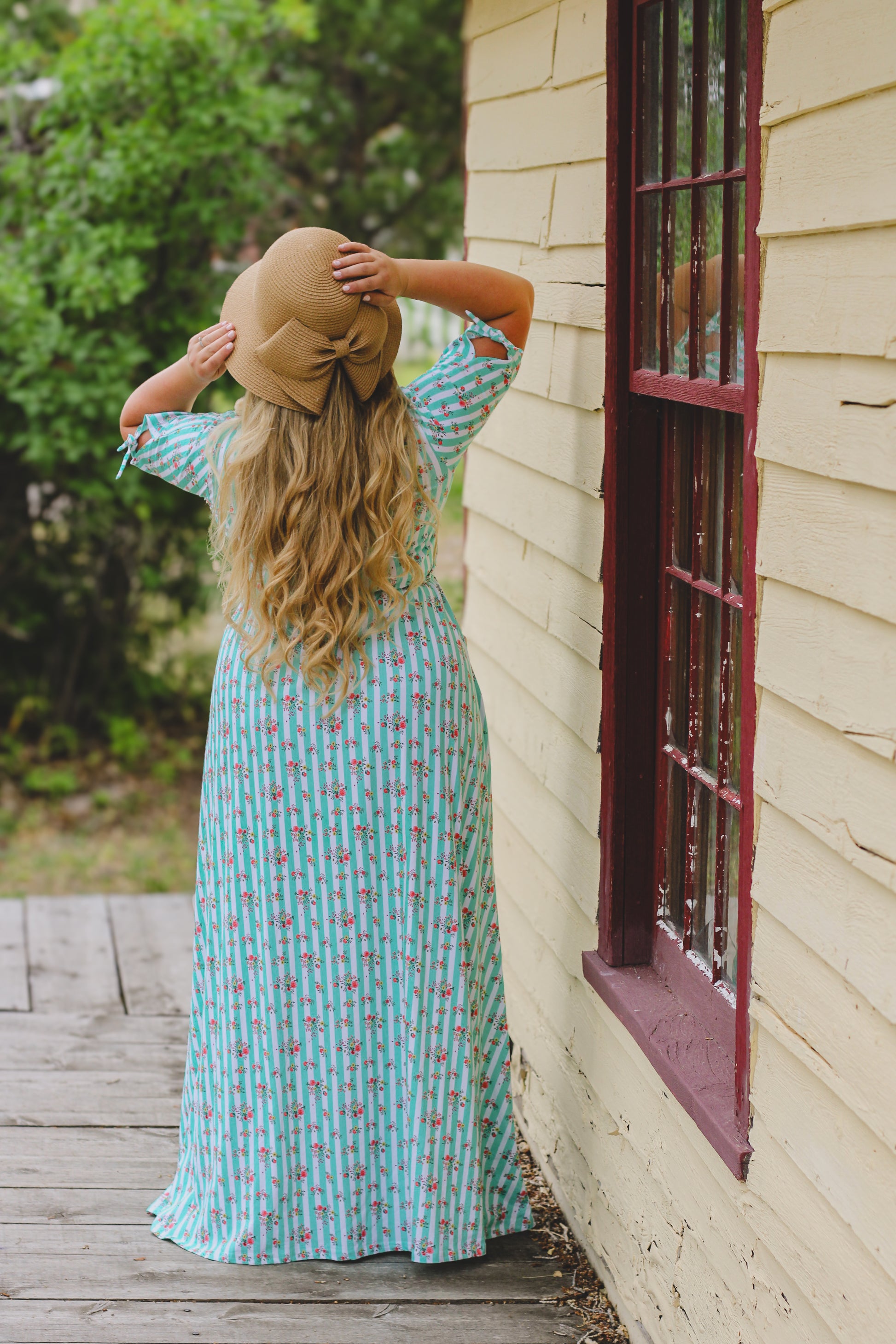 Woman in a long modest nursing dress standing by a window of a house