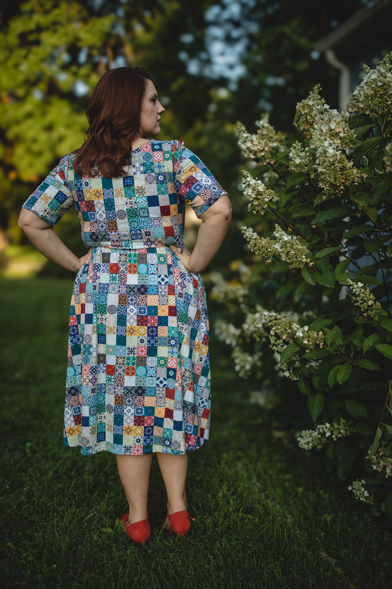 Woman wearing a colorful patchwork modest nursing dress standing outdoors with greenery around