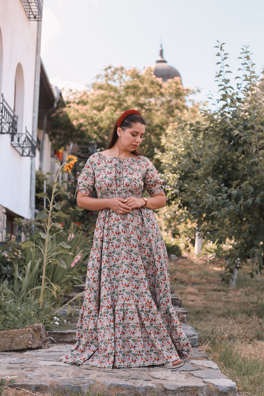 Woman in a floral modest nursing dress standing outdoors with trees and a building in the background