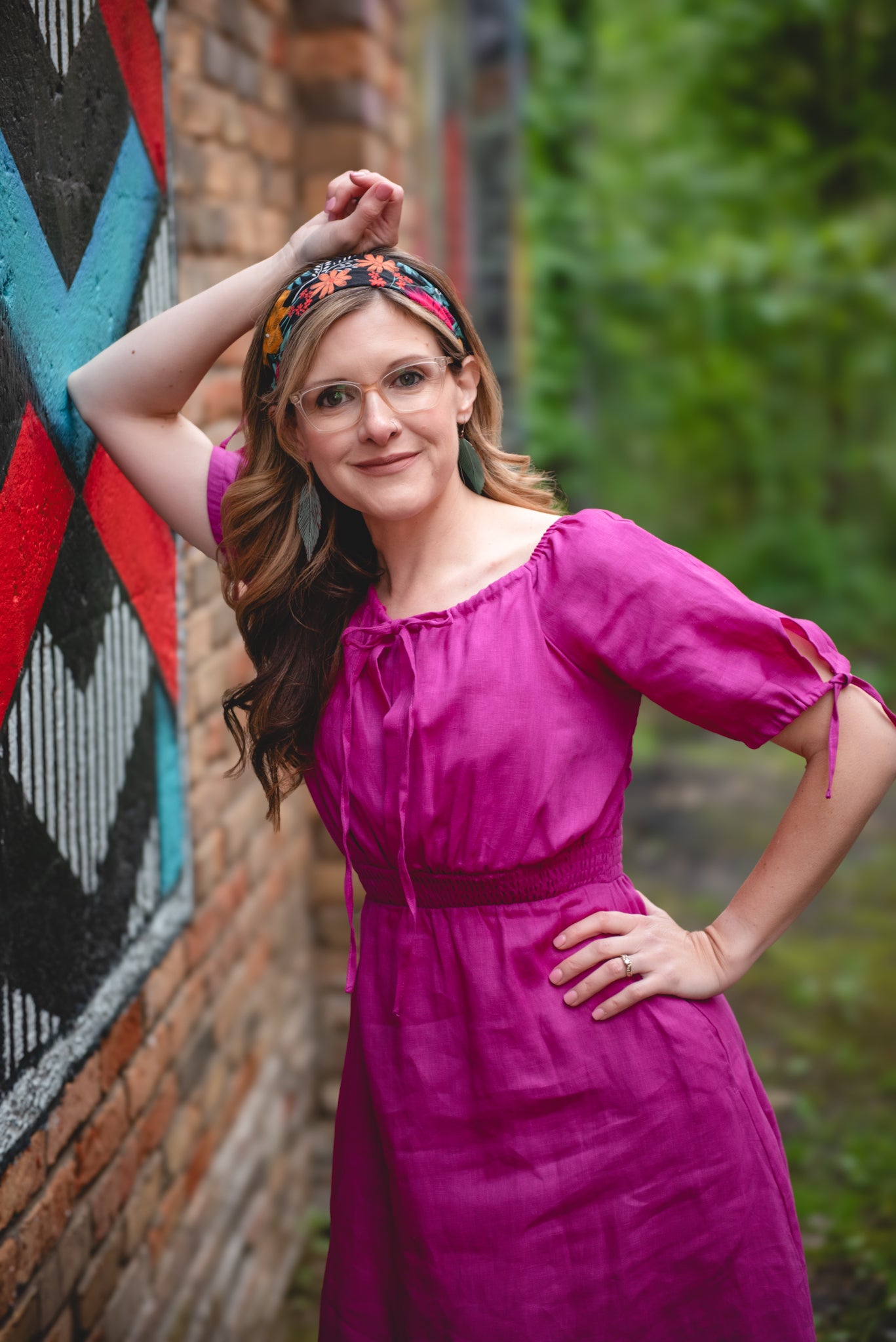 Woman in a pink modest nursing dress posing against a brick wall with graffiti