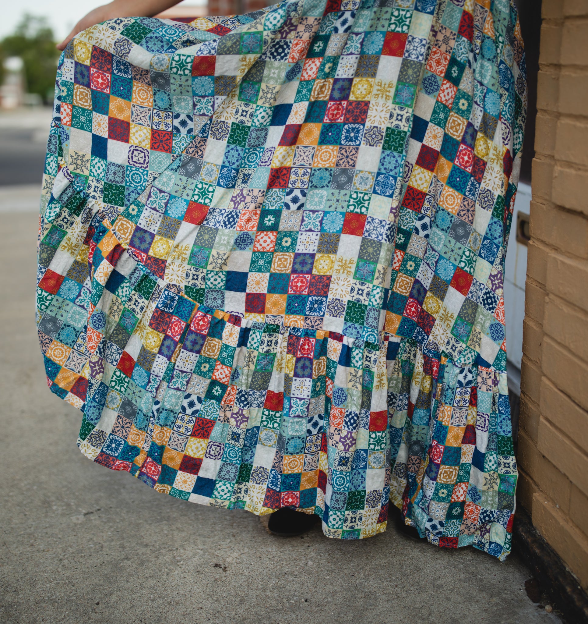 Person wearing a colorful patchwork modest nursing dress standing on a sidewalk.