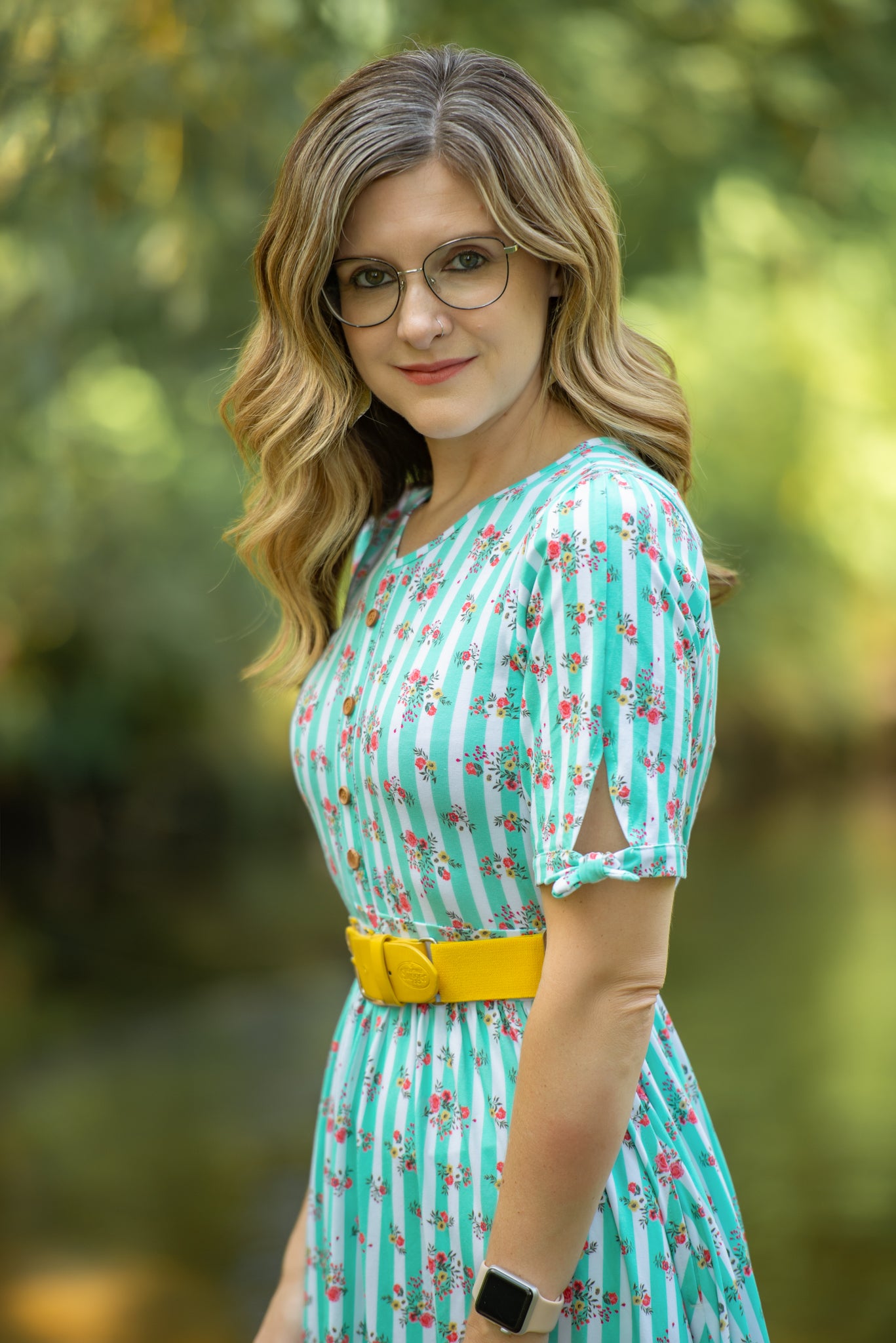 Woman wearing a green floral modest nursing dress with a yellow belt in a blurred outdoor setting
