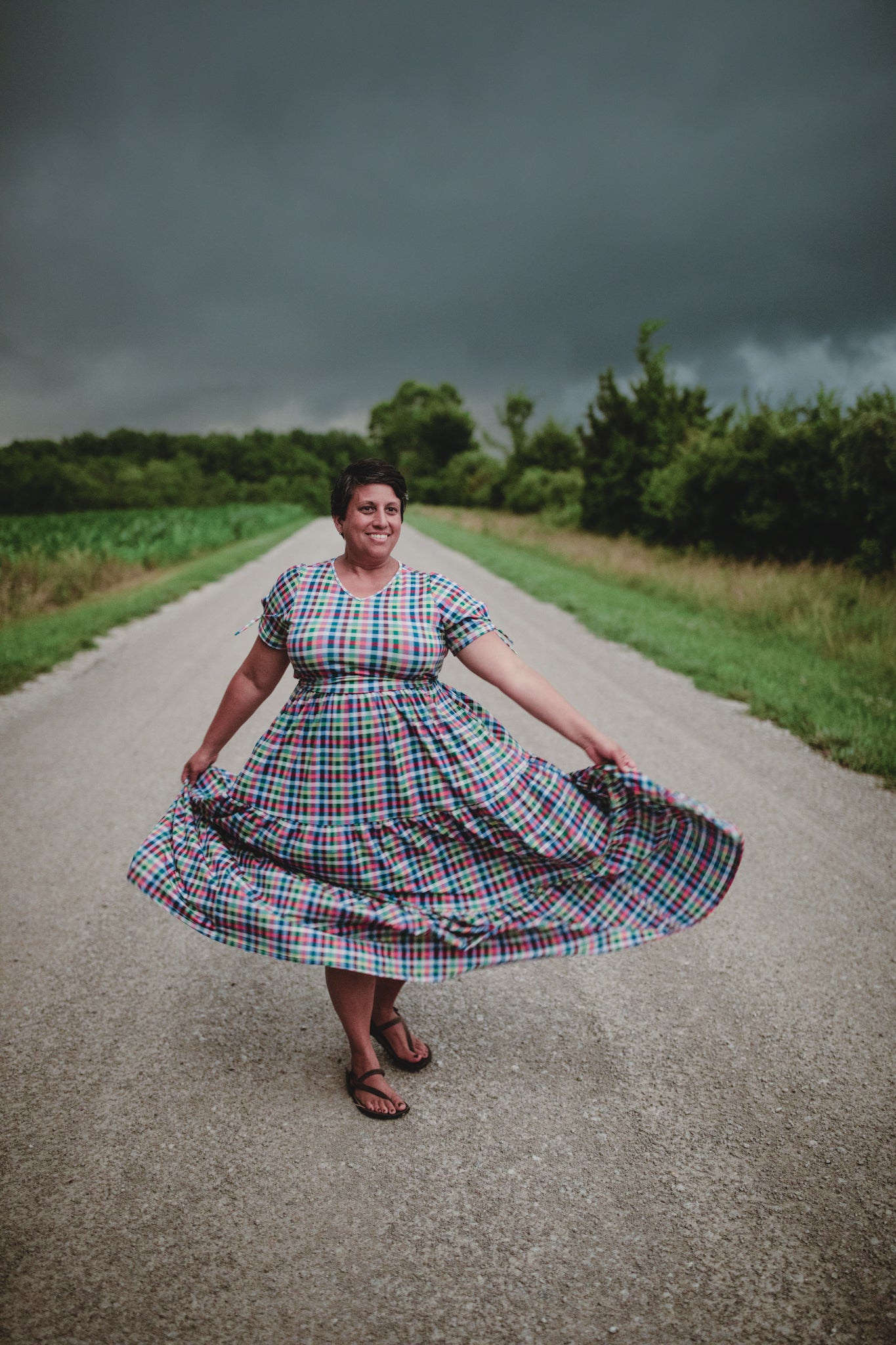 Woman in a plaid modest nursing dress standing on a road with a stormy sky