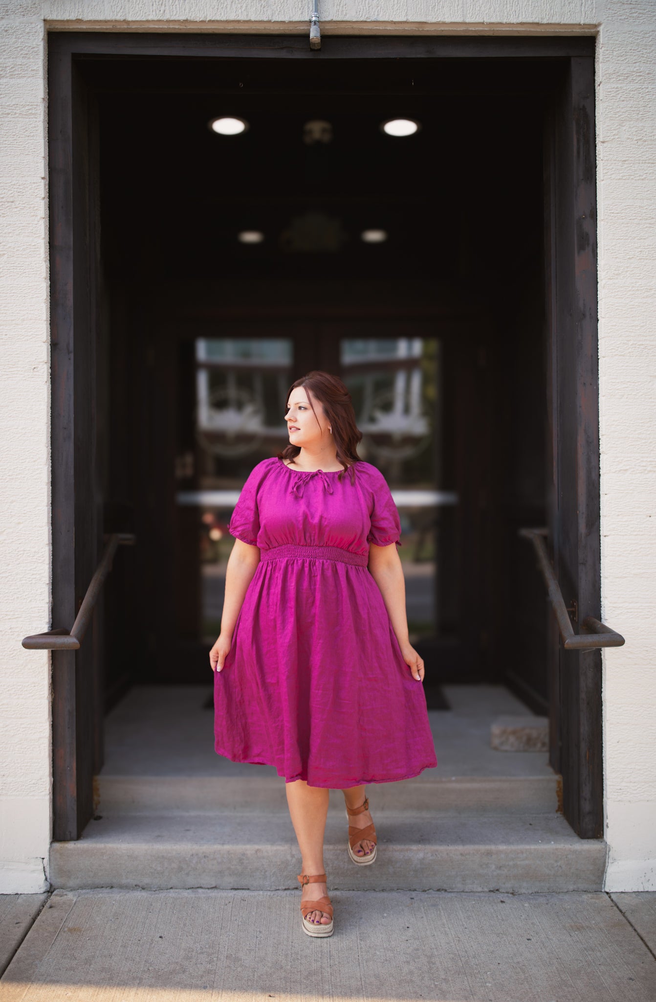 Woman in a pink modest nursing dress standing in an open doorway.