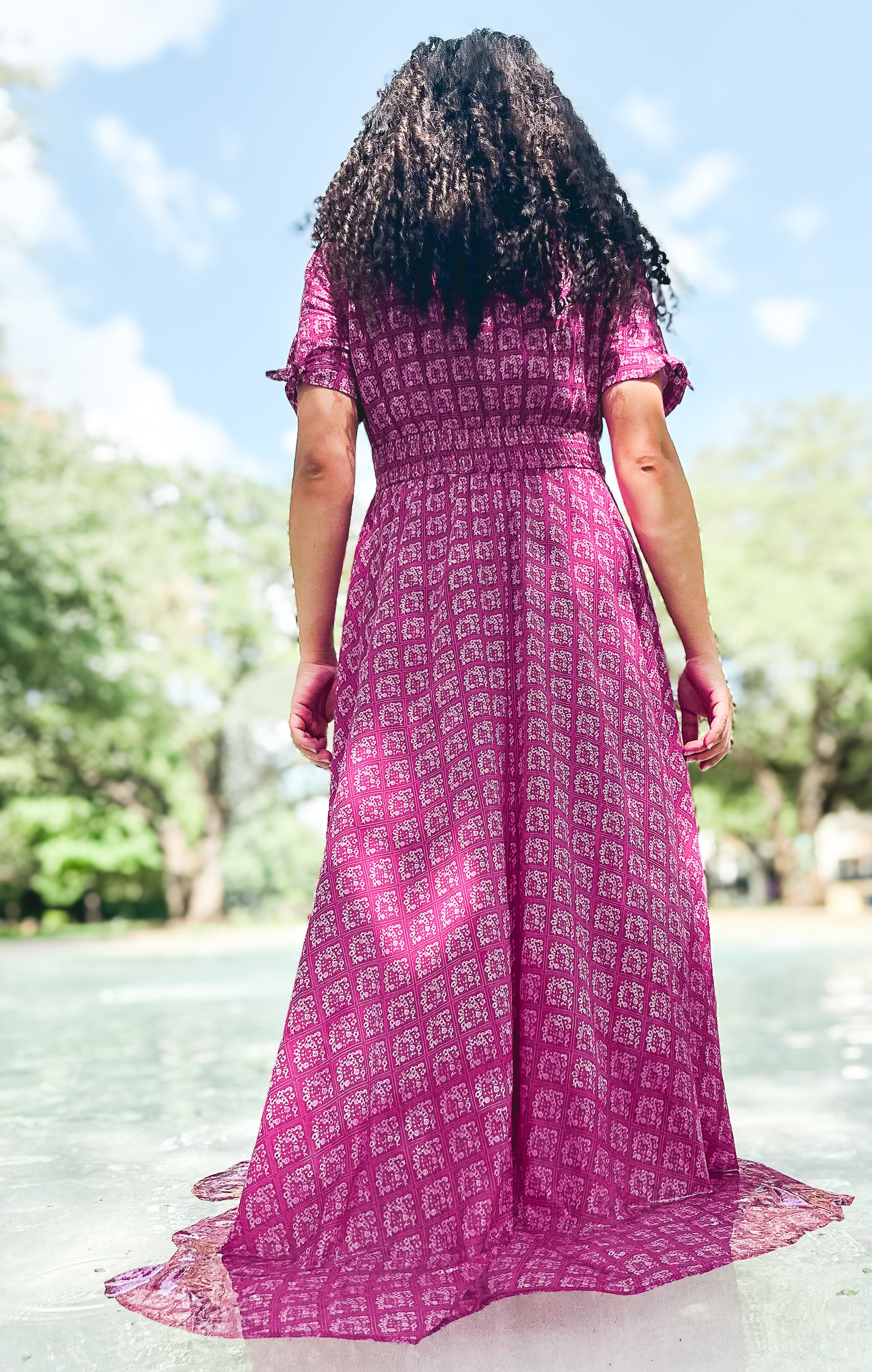 Person wearing a pink modest nursing dress with a pattern, standing by a pool with trees in the background