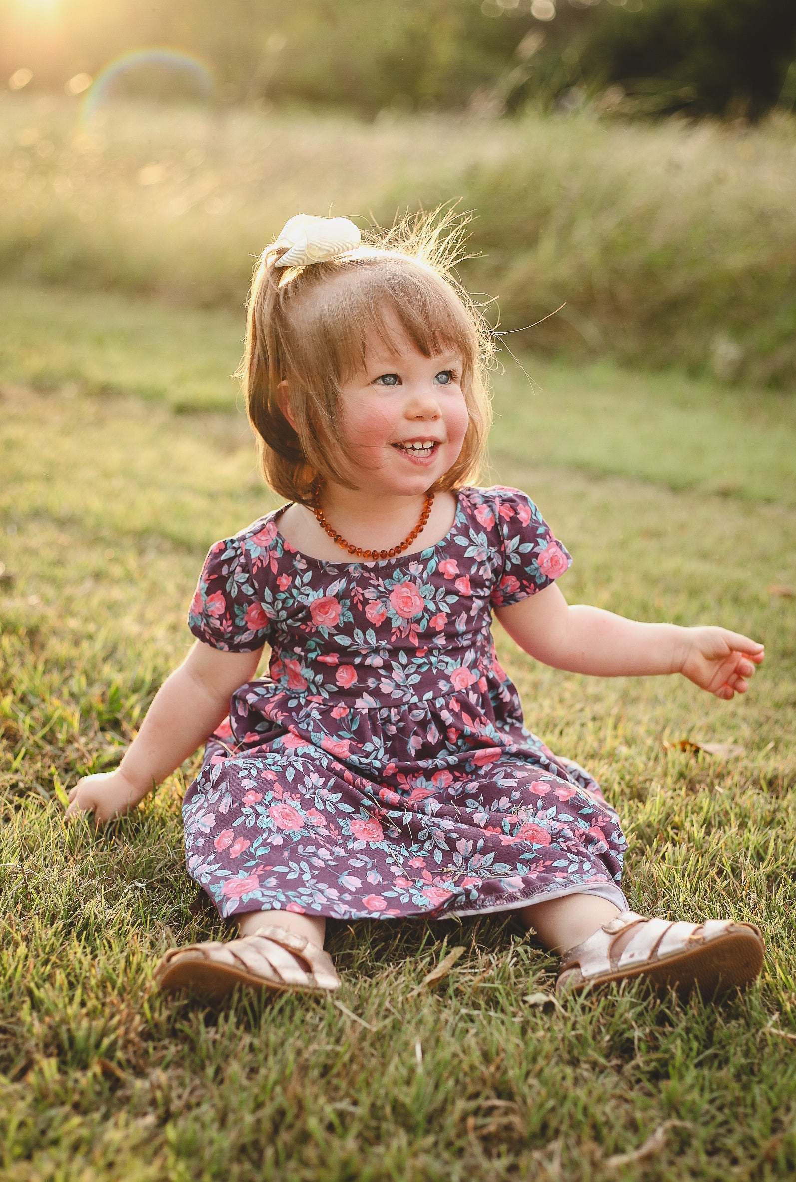 Child in floral dress sitting on grass