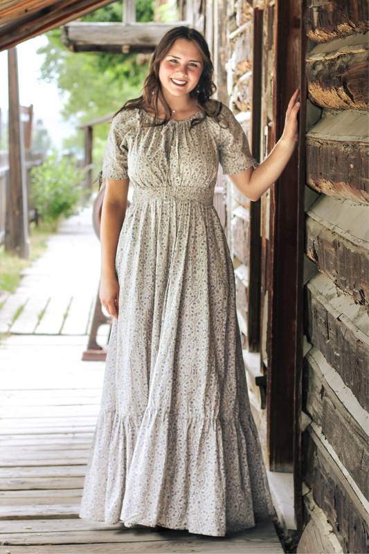 Woman in patterned modest nursing dress standing on a wooden porch.