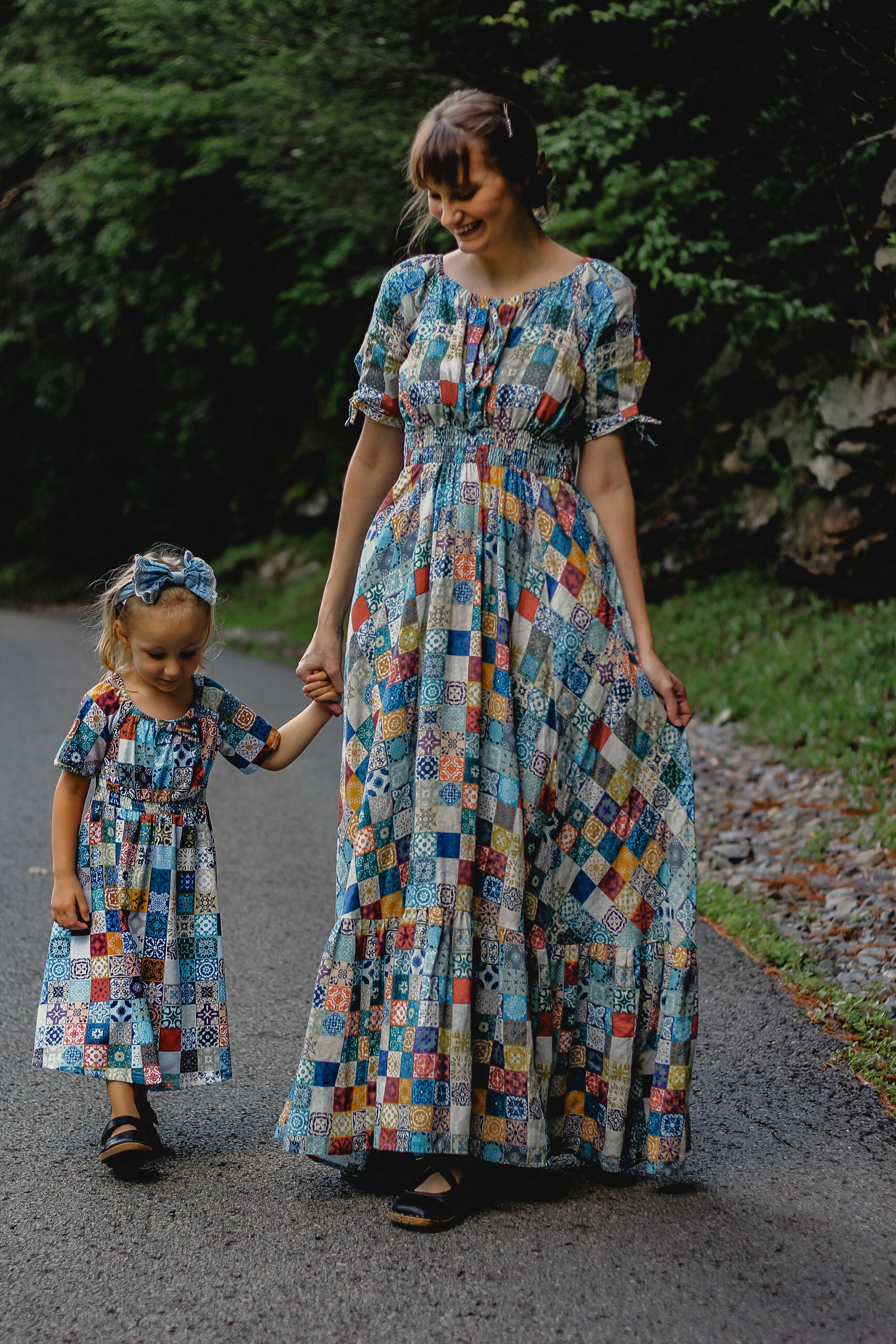 Woman and child in matching colorful patchwork modest dresses walking on a path.