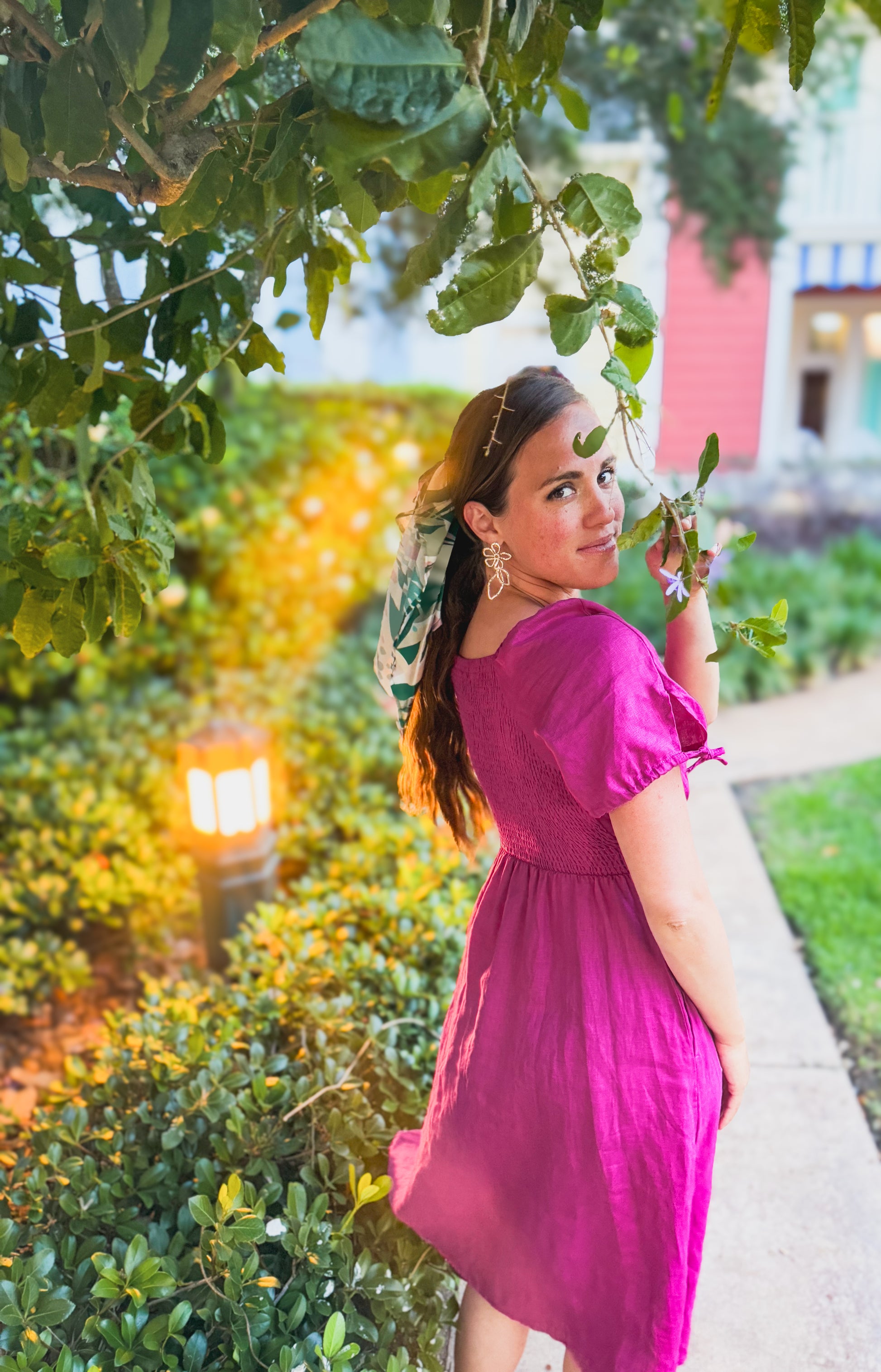 Woman in a pink modest nursing dress standing among greenery with a blurred background