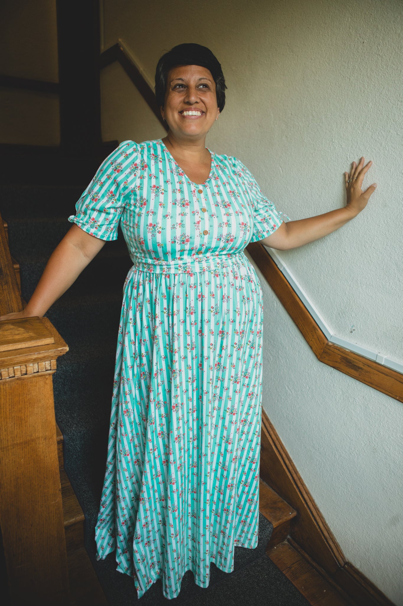 Woman in a green patterned modest nursing dress standing on a staircase.
