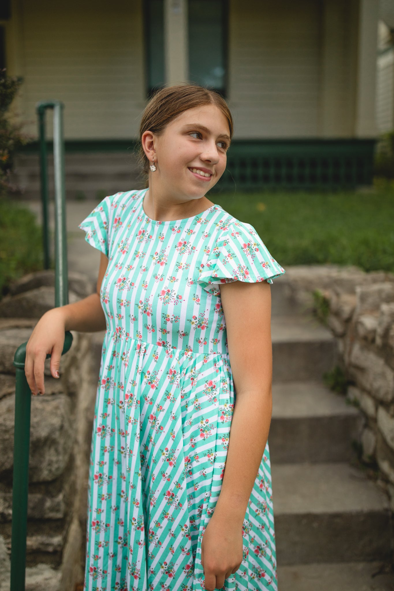 Young girl in a teal modest dress with floral pattern standing outdoors.