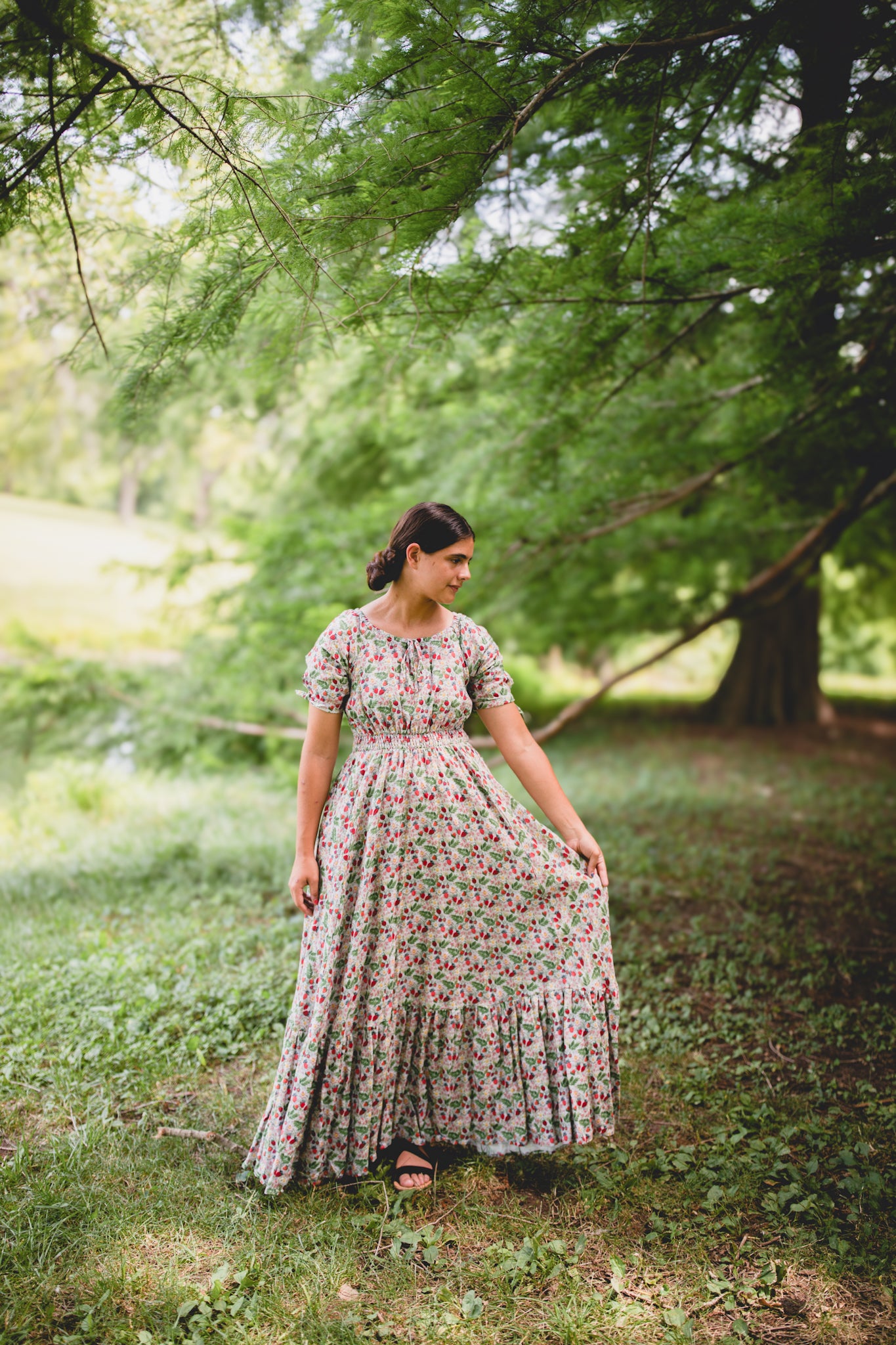 Woman in a floral modest nursing dress standing in a park with trees and grass.