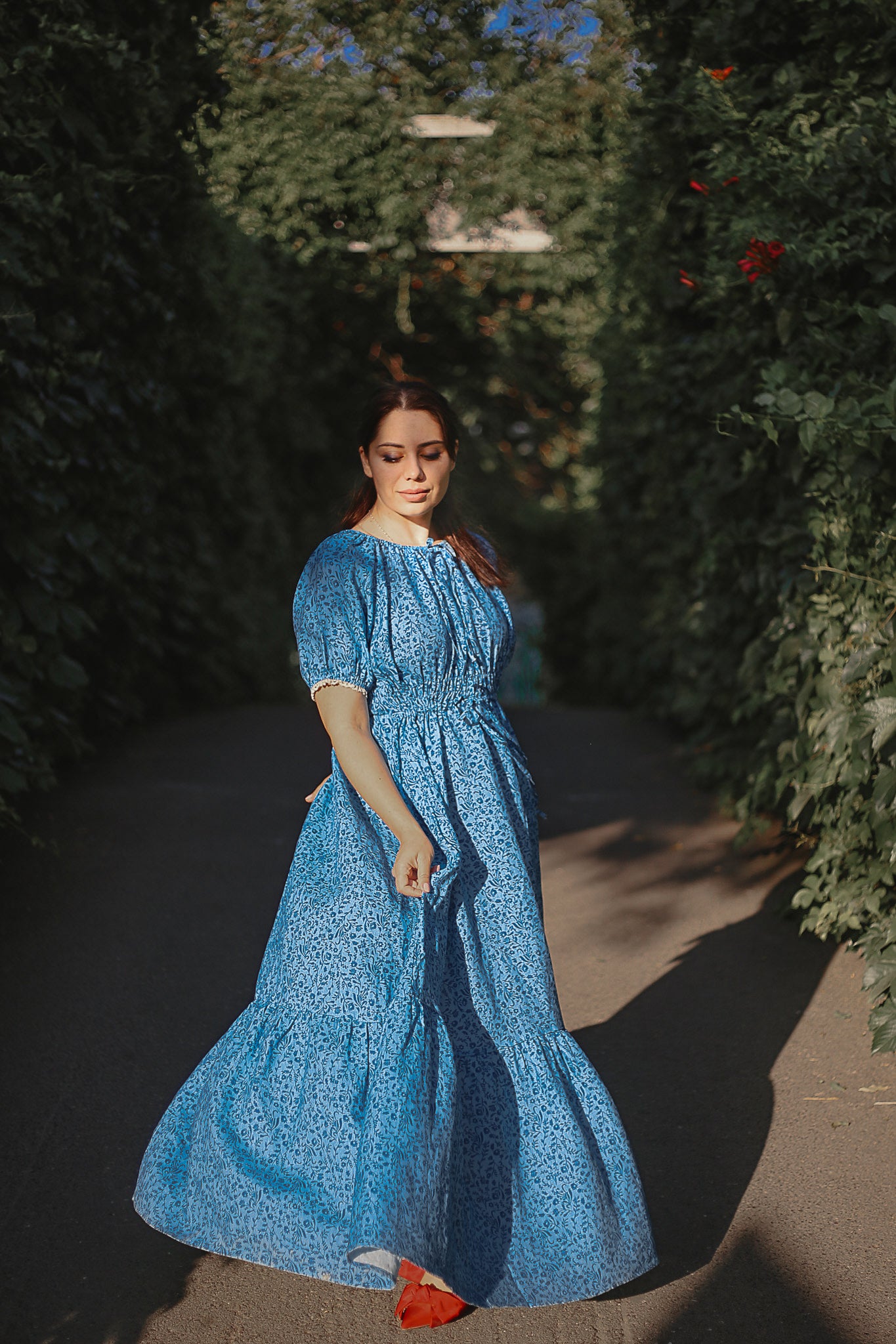 Woman in a blue modest nursing dress standing in a sunlit garden