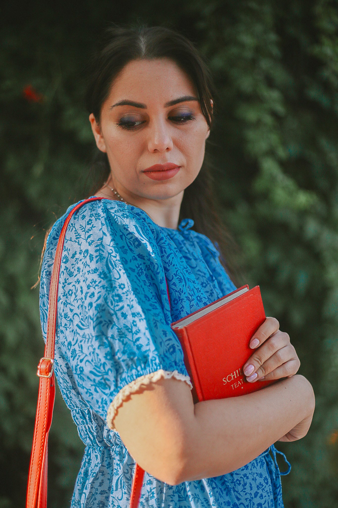 Woman in a blue modest nursing dress holding a red notebook with a blurred green background