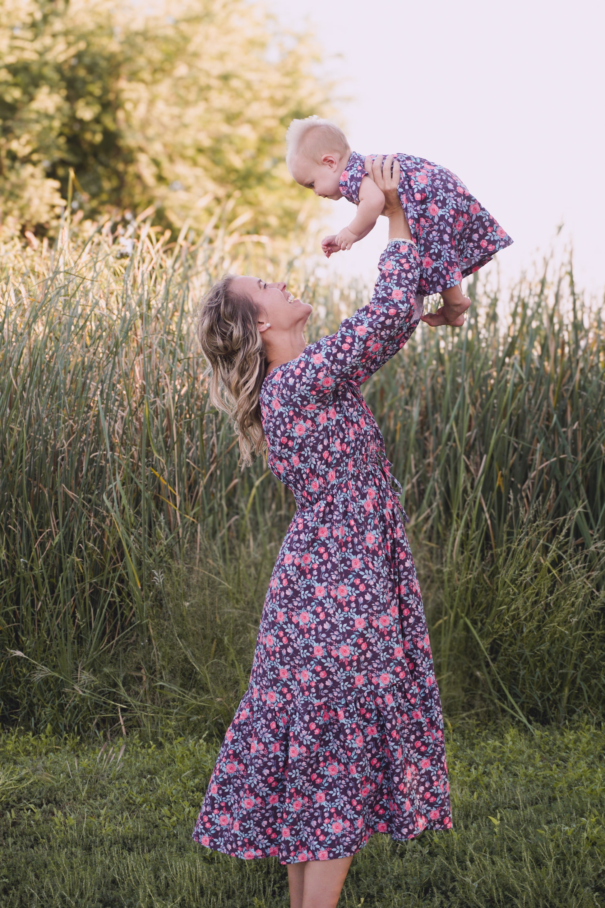 Woman in modest nursing floral dress holding baby in field