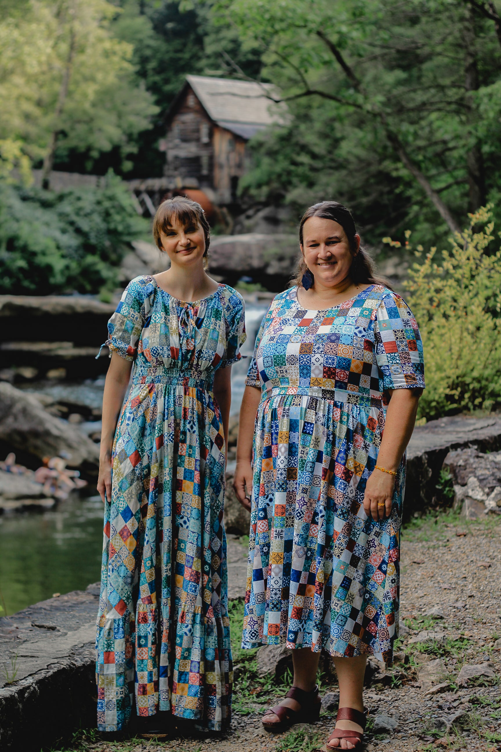 Two women in colorful patterned modest nursing dresses standing outdoors with a natural background.