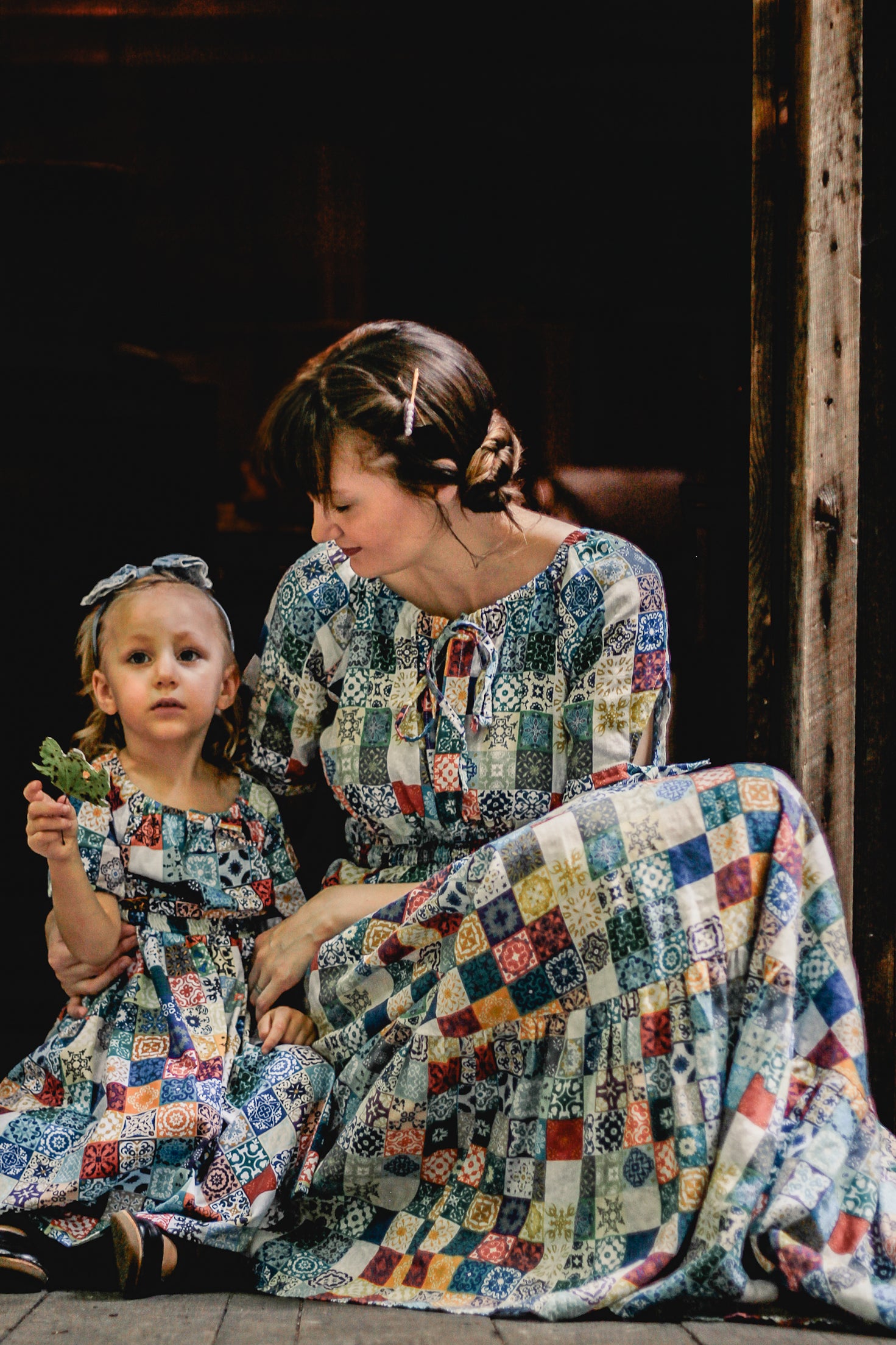 Woman and child in patchwork modest dresses sitting together outdoors.