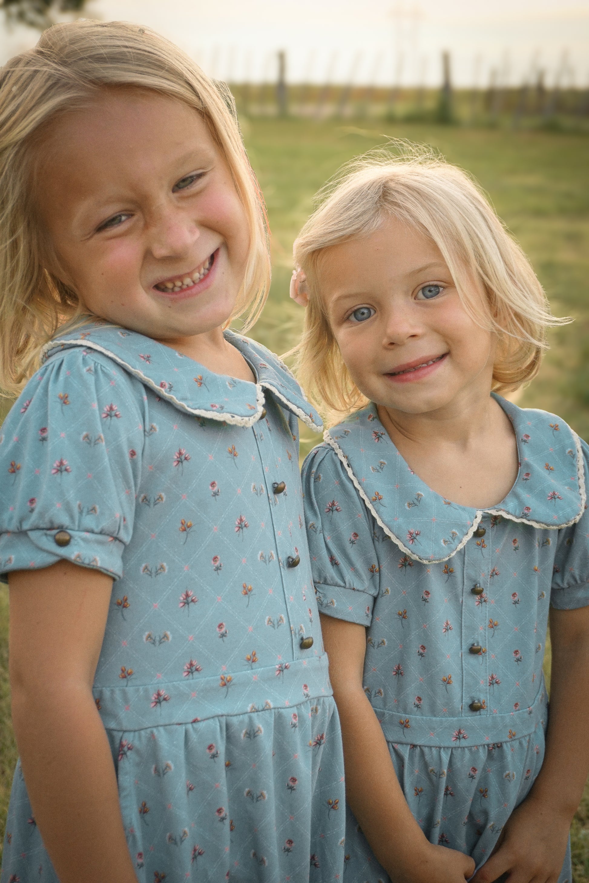 Two young girls in matching blue dresses standing outdoors.