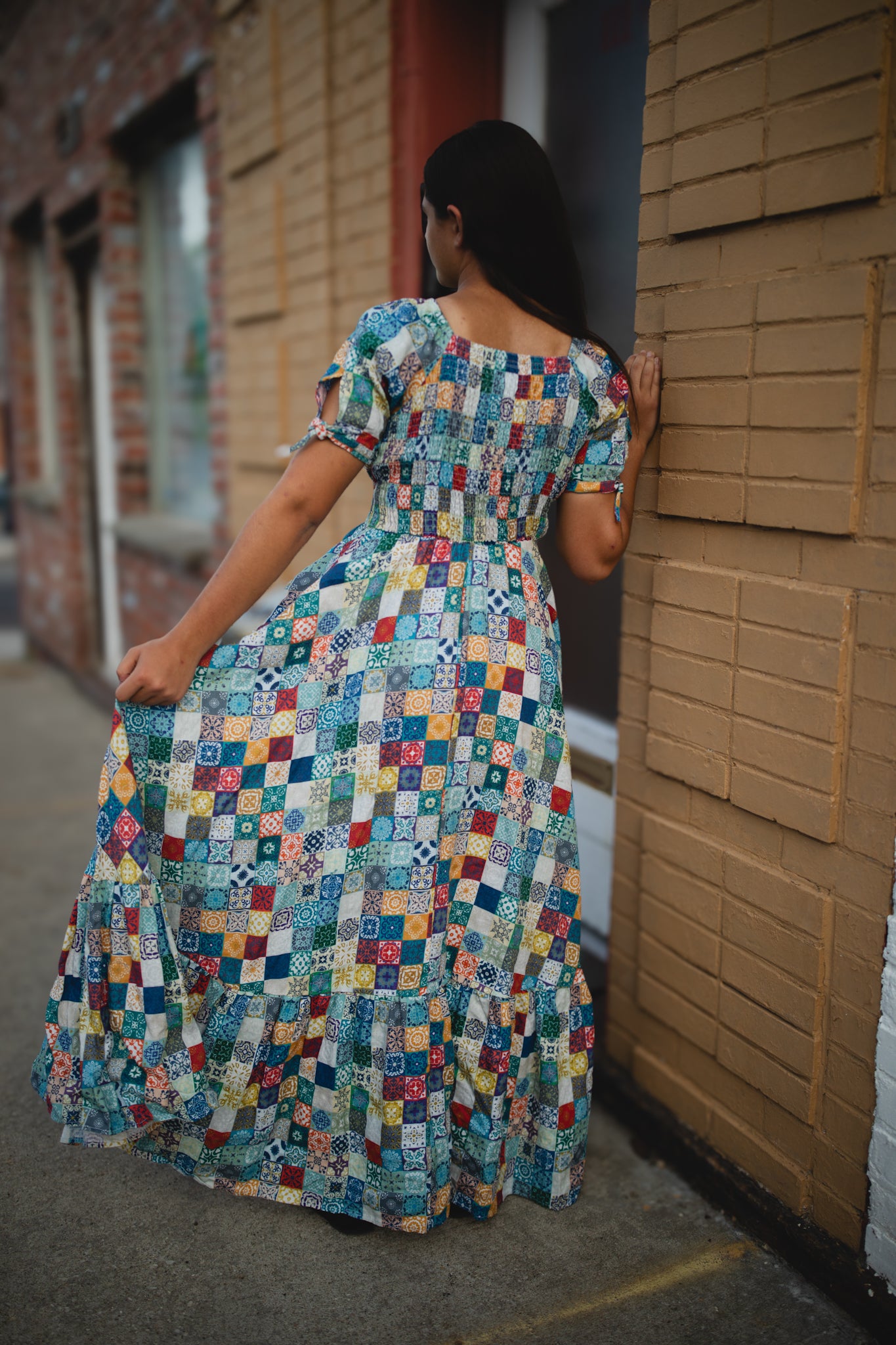 Woman in a colorful modest nursing dress standing against a brick wall.