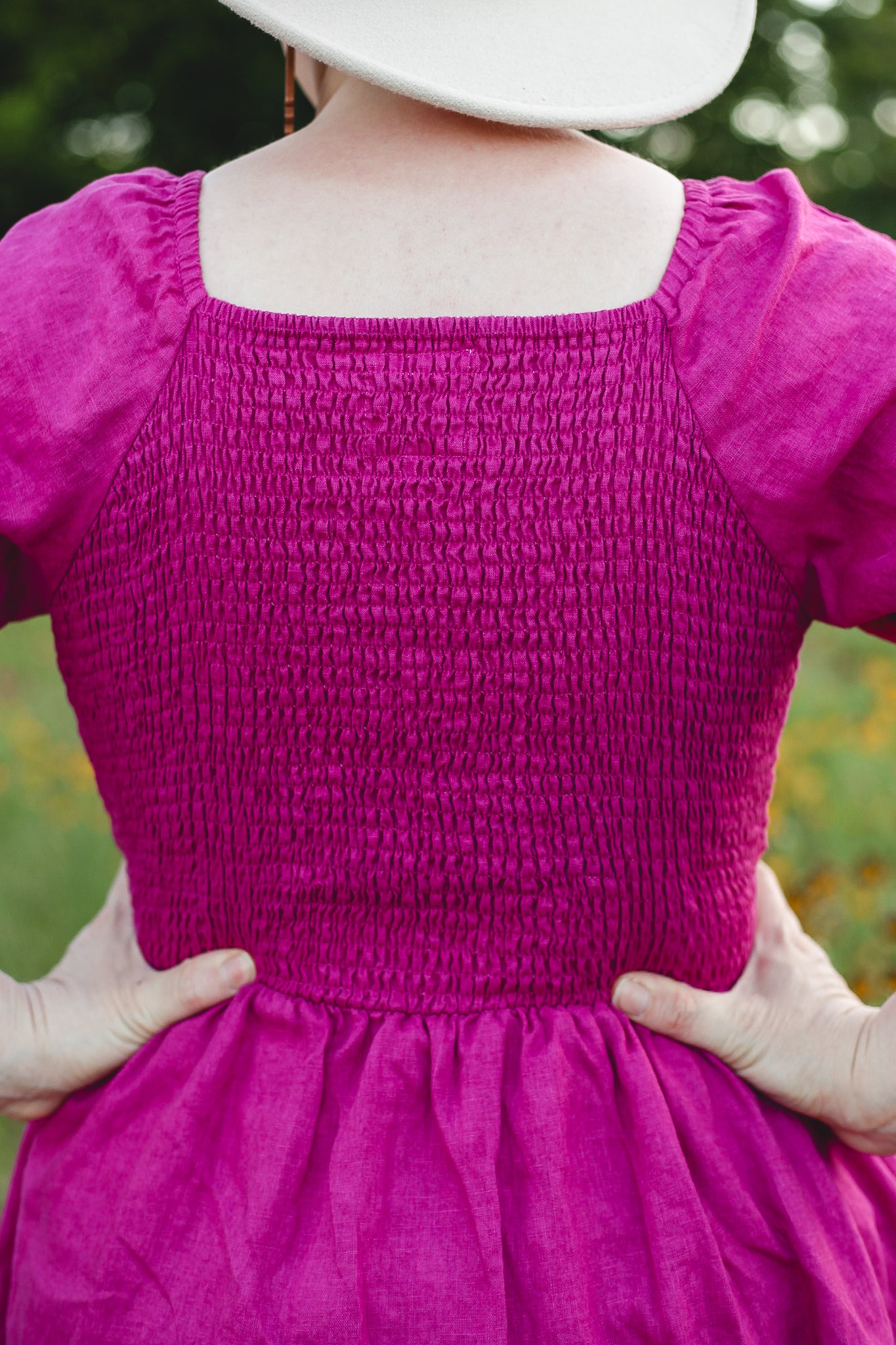Person wearing a pink modest nursing dress with smocked bodice and plain skirt against a blurred natural background