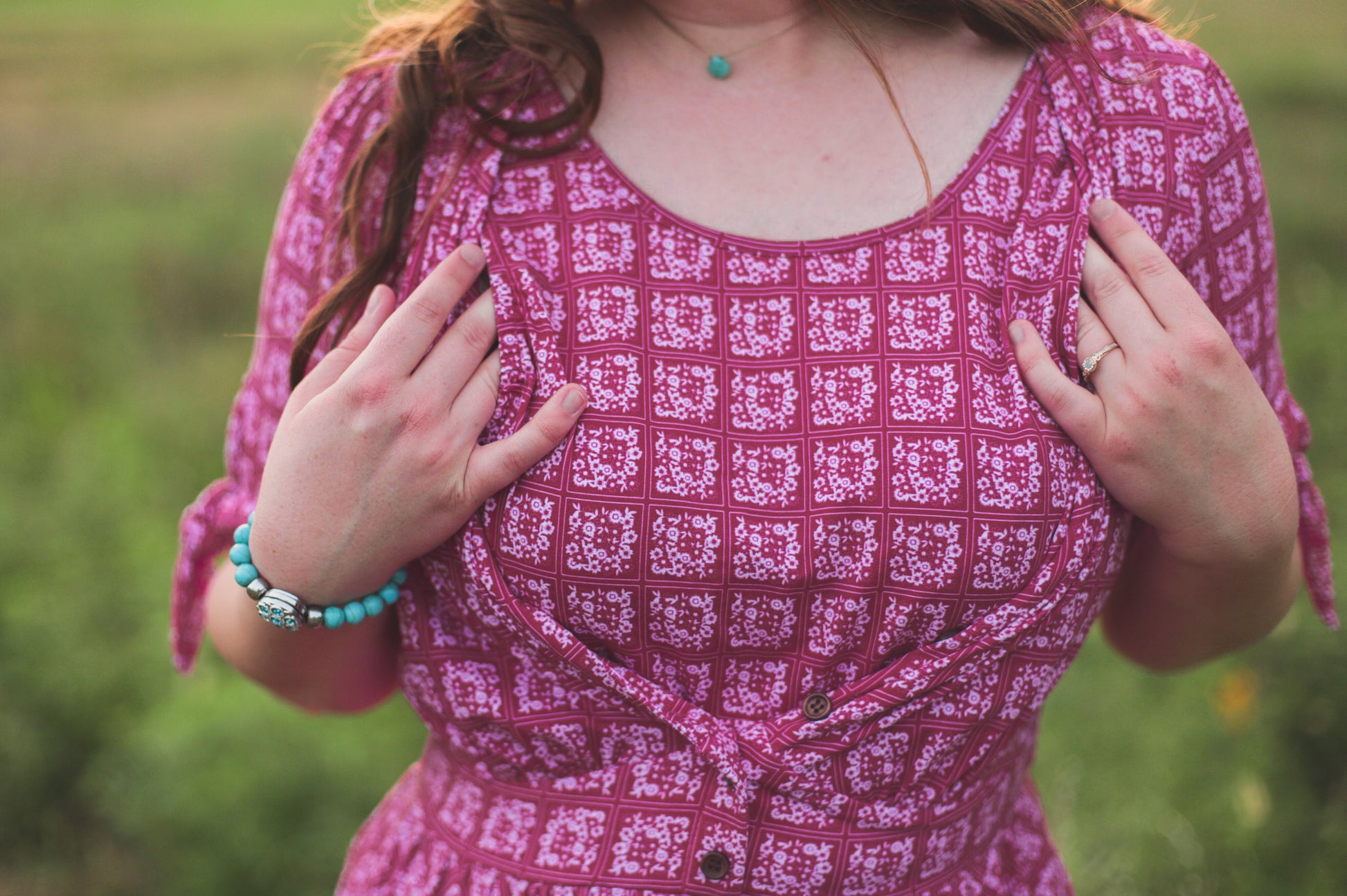 Person wearing a pink patterned modest nursing dress with a blurred green background