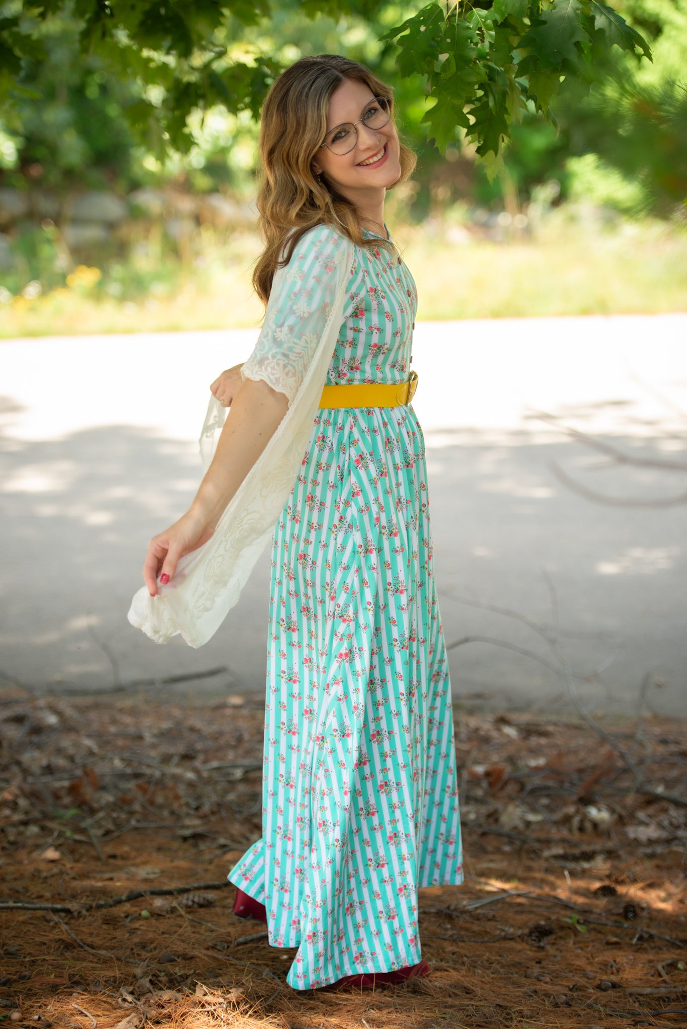 Woman in a long, patterned modest nursing dress standing outdoors with greenery in the background