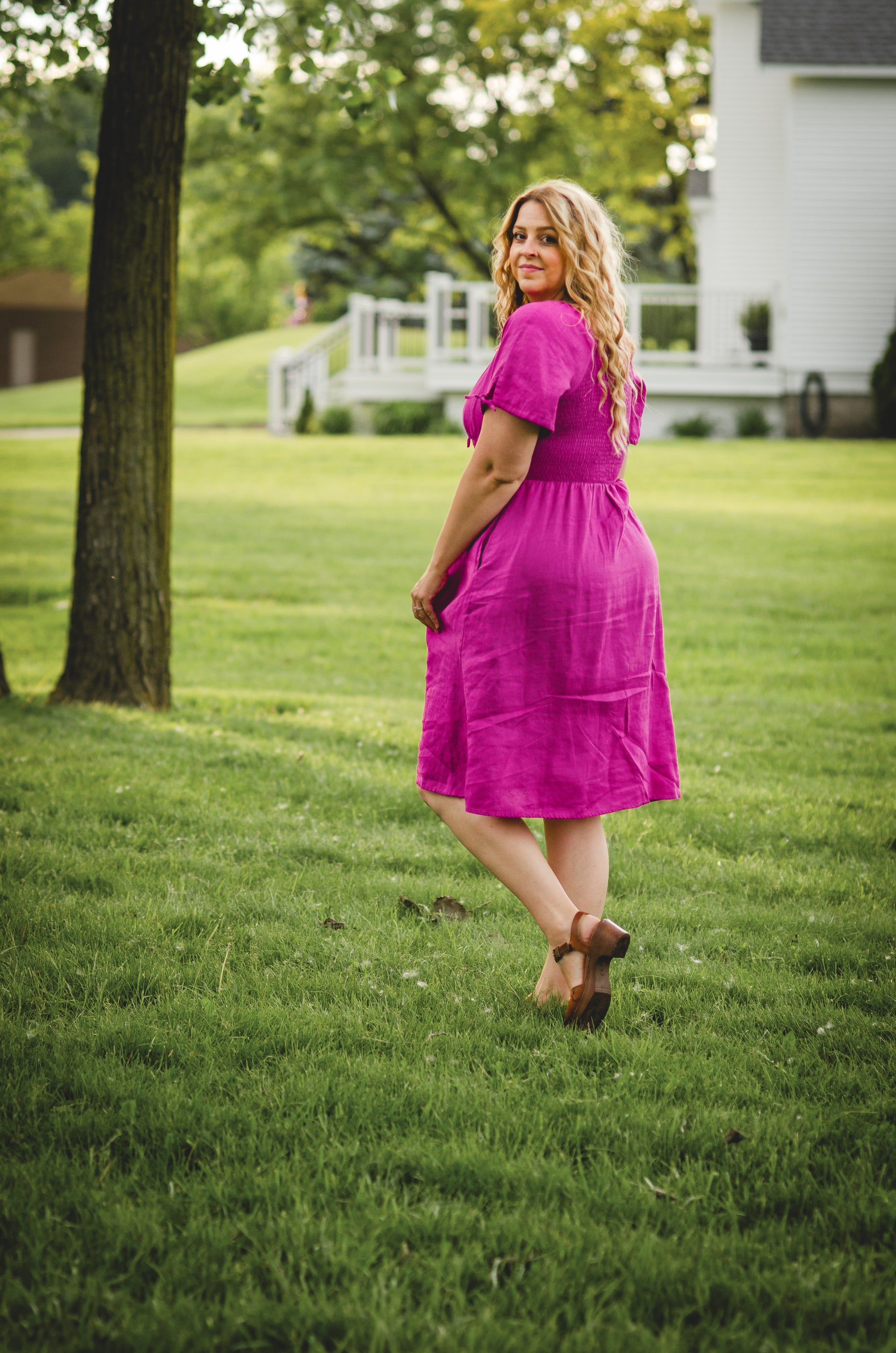 Woman in a pink modest nursing dress standing on grass with a house in the background