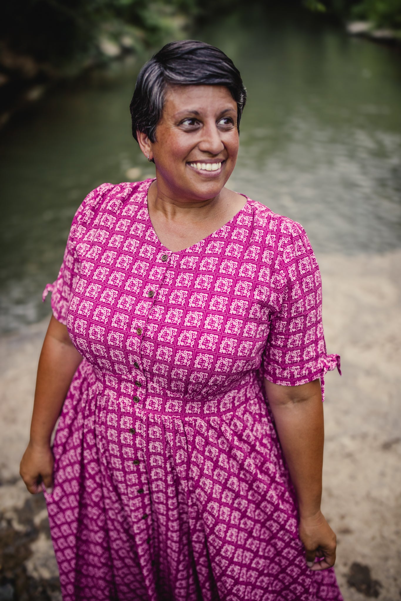 Woman in a pink patterned modest nursing dress standing by a body of water.