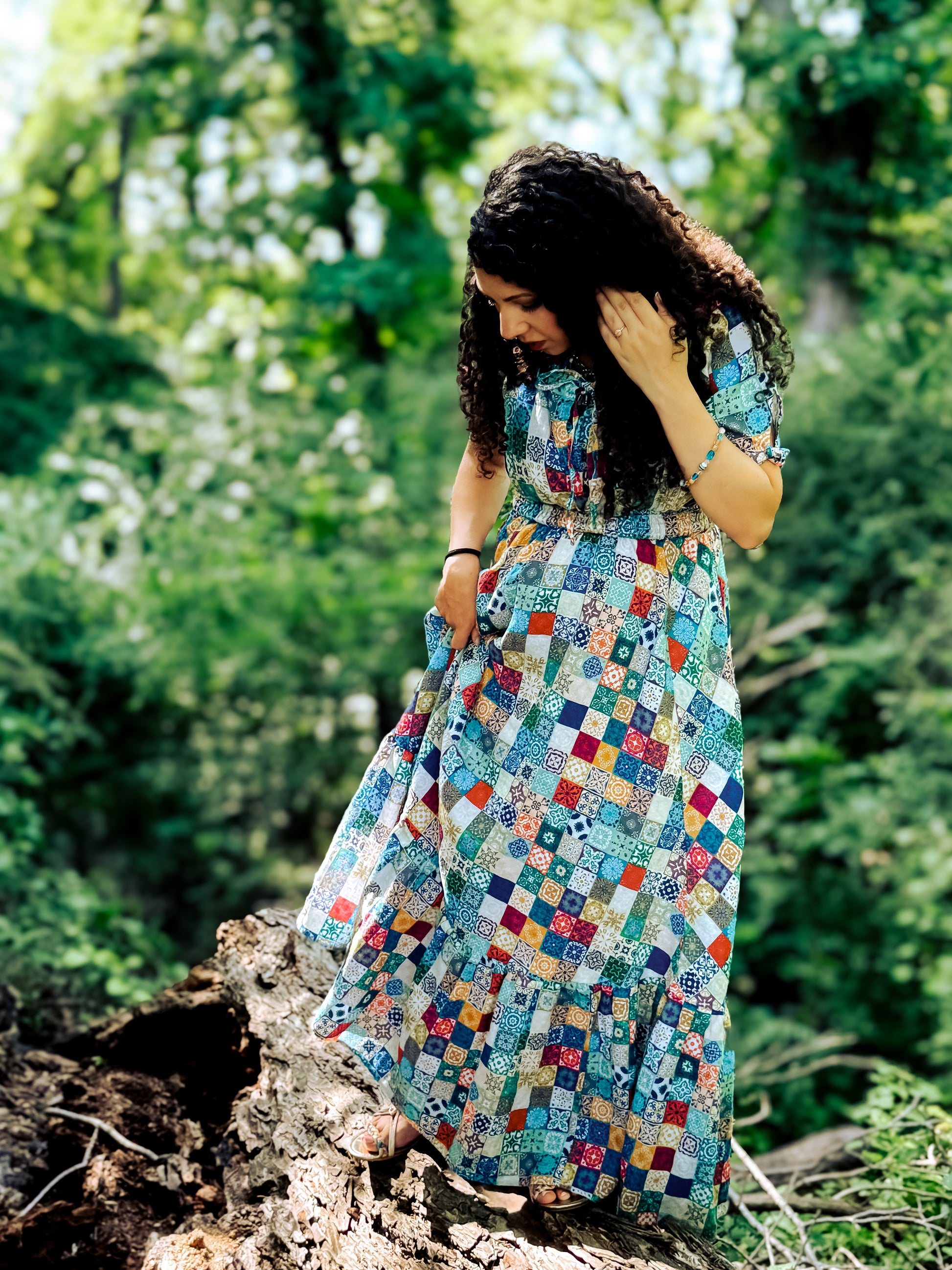 Woman in a colorful patchwork modest nursing dress standing on a log in a forest