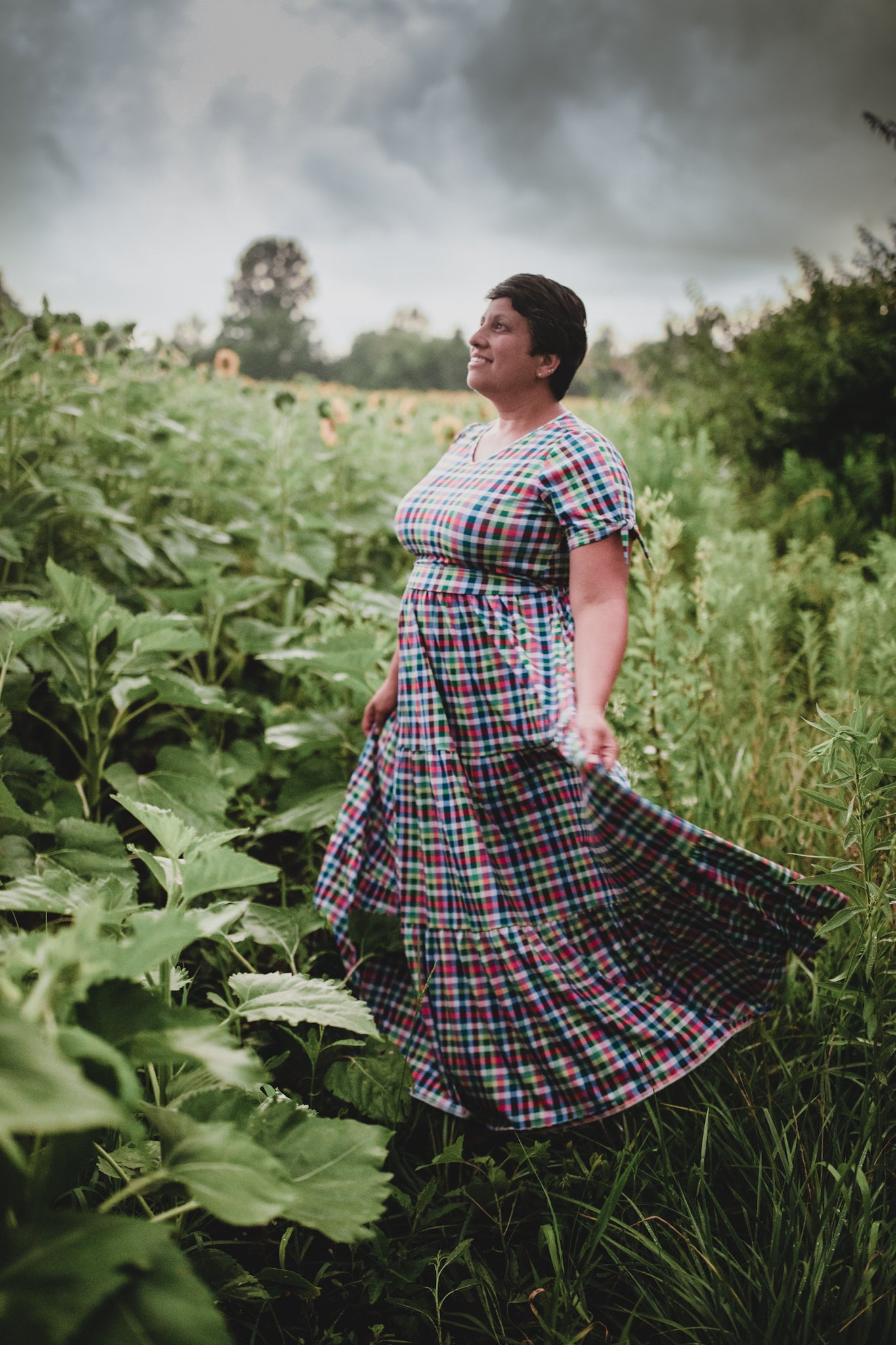 Woman in a plaid modest nursing dress standing in a field with stormy skies.