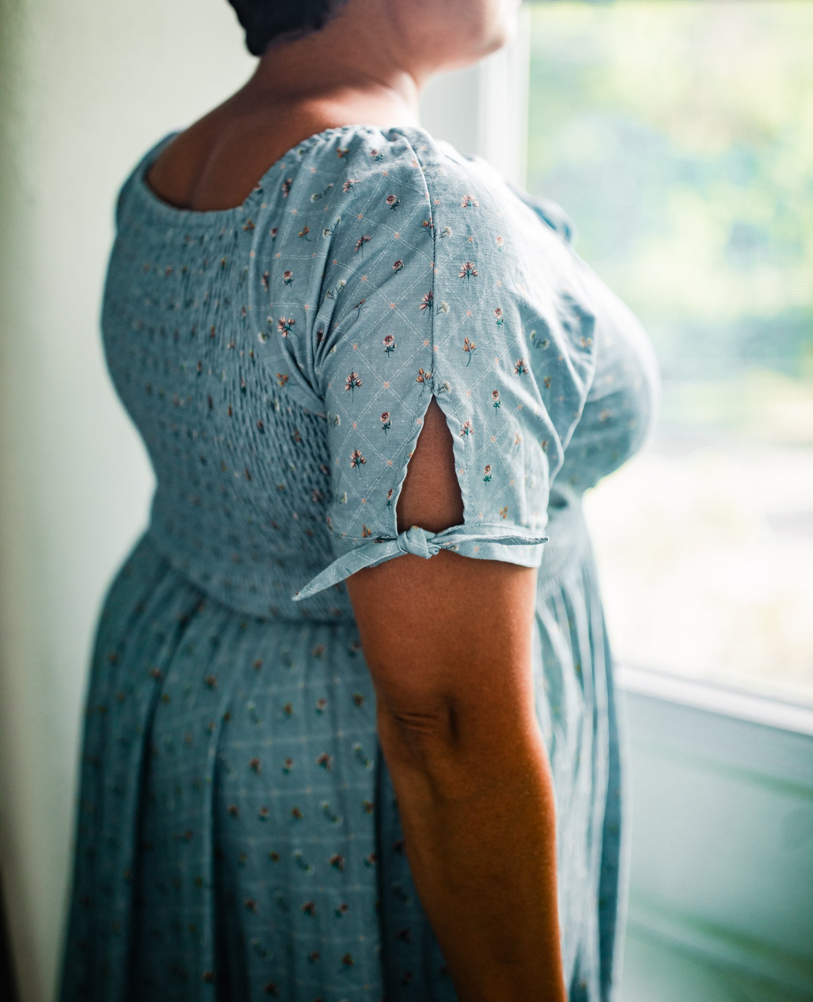 Person wearing a light blue modest nursing dress with floral pattern in a softly blurred indoor setting