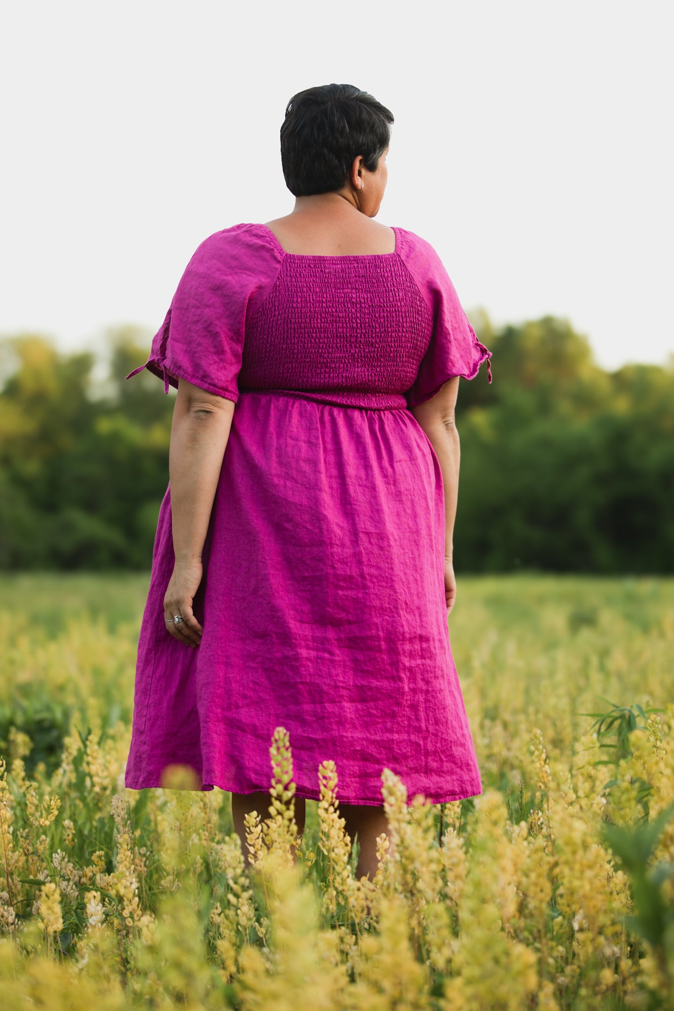 Person wearing a pink modest nursing dress standing in a field with greenery in the background